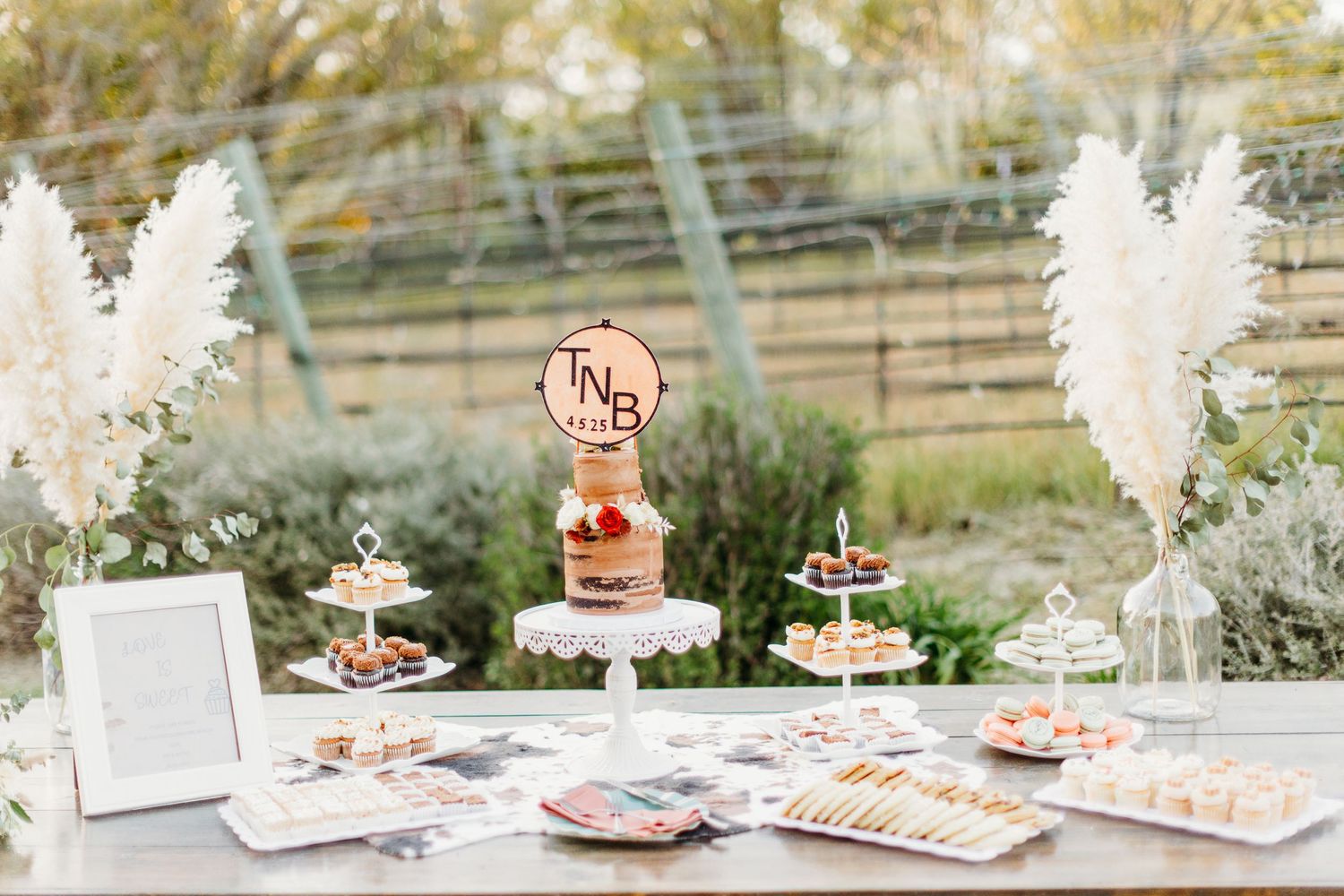 Rustic wedding dessert table with pampas grass decorations and tiered cake display.