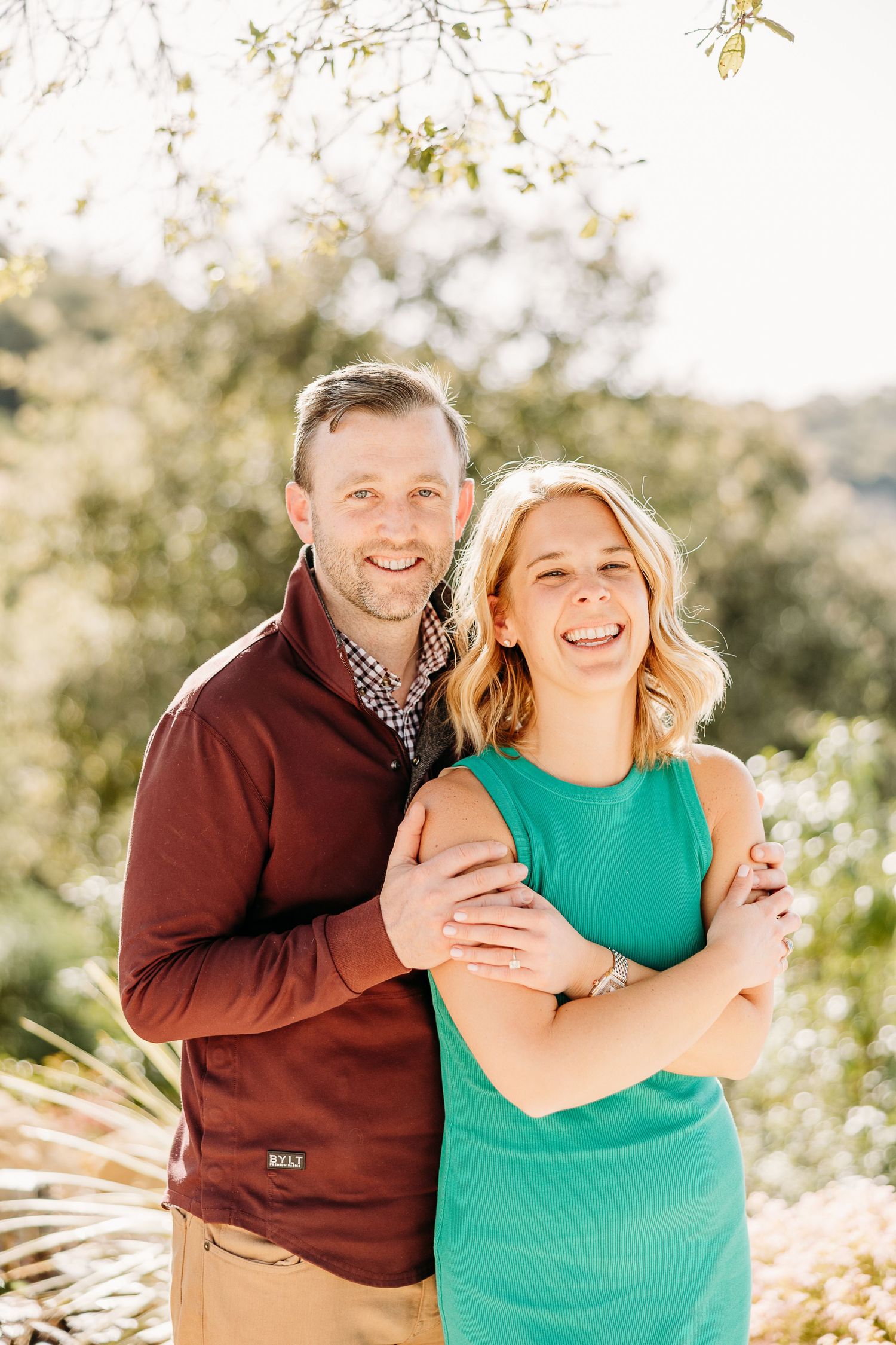A couple shares loving embraces while wearing brown and green outfits during an outdoor photoshoot.