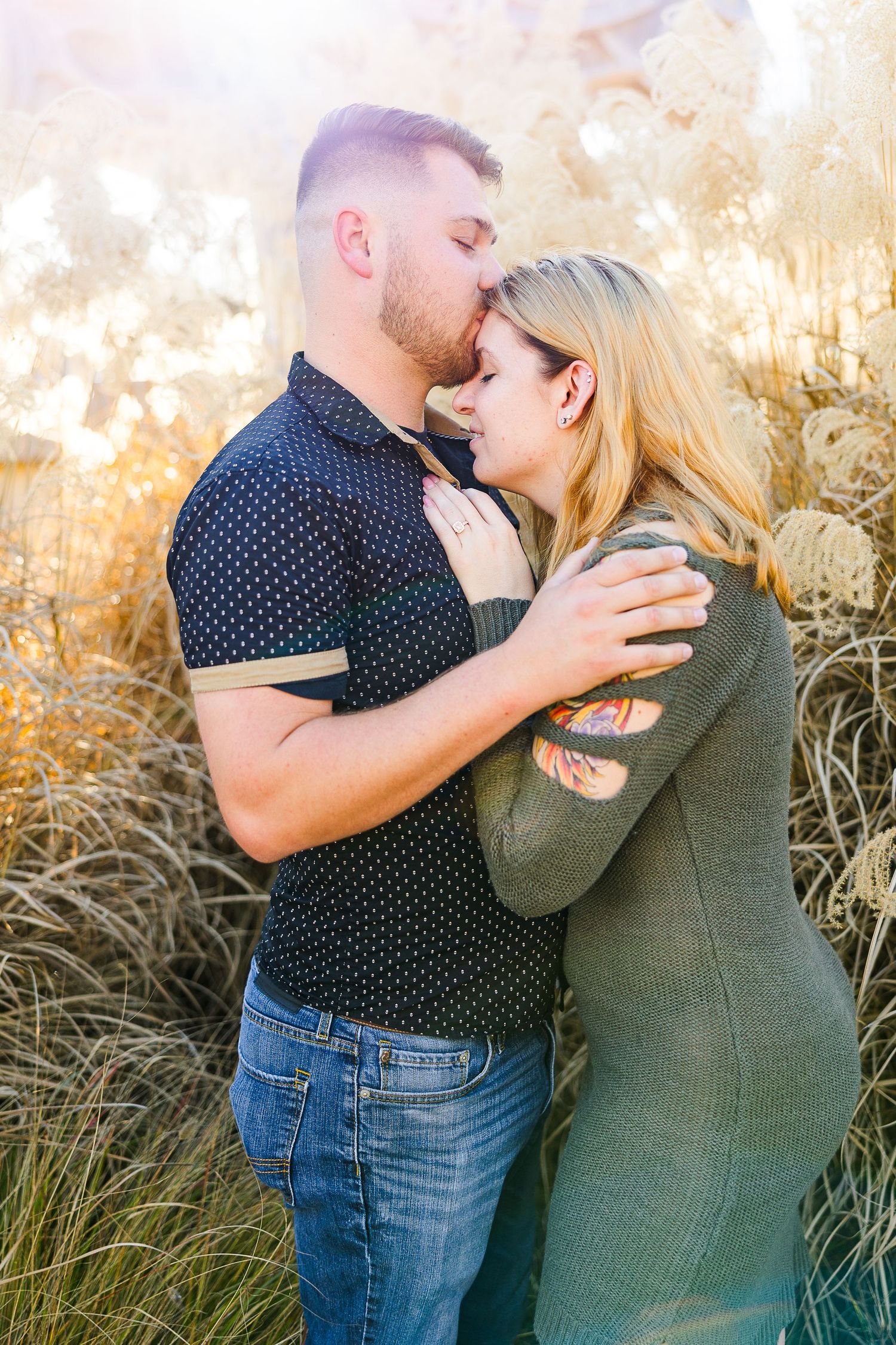 A couple embraces in warm sunlight among tall golden grasses during sunset.