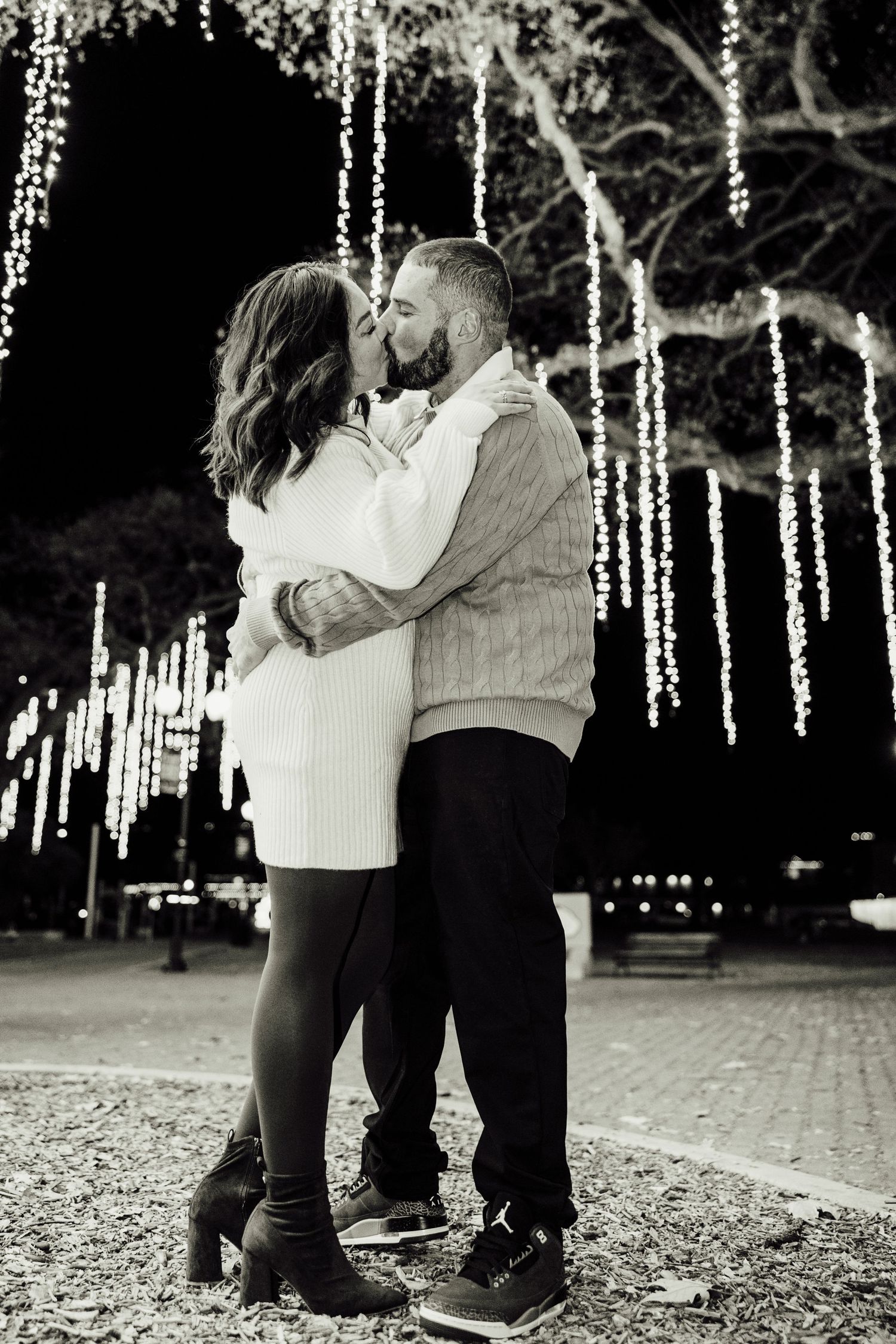 A romantic black and white photo series of a couple embracing under twinkling string lights in a park setting.