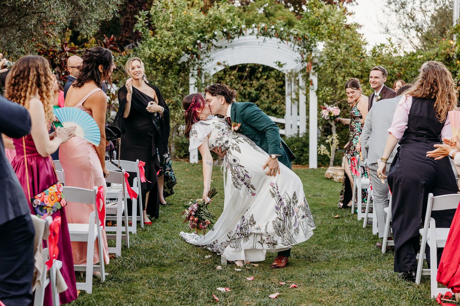 Wedding guests dance together on a grassy lawn during an outdoor reception celebration.