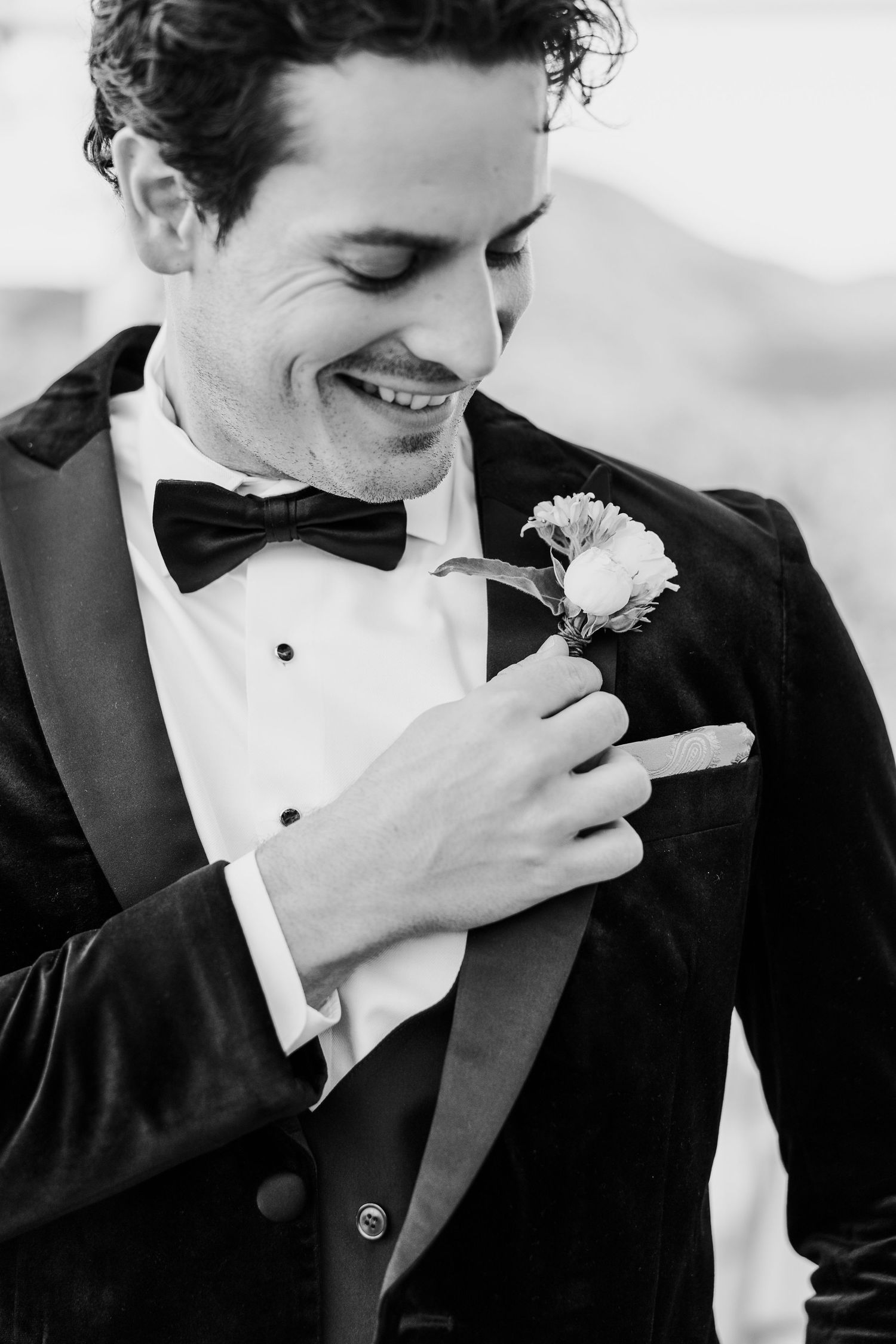Close-up series of a groom in black tuxedo adjusting his boutonniere with a joyful smile.