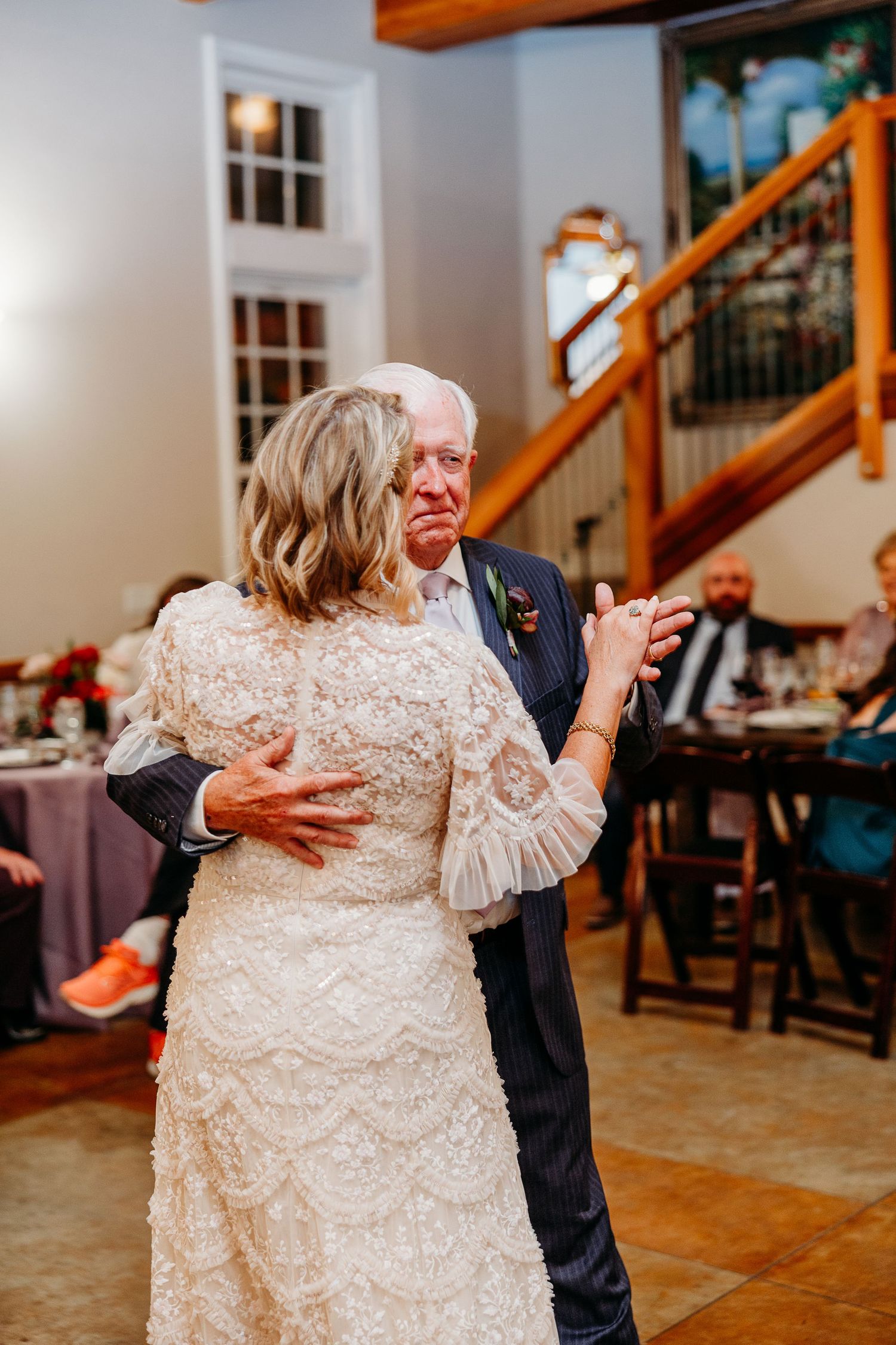 Couple dancing together in white lace dress and dark suit at indoor reception.