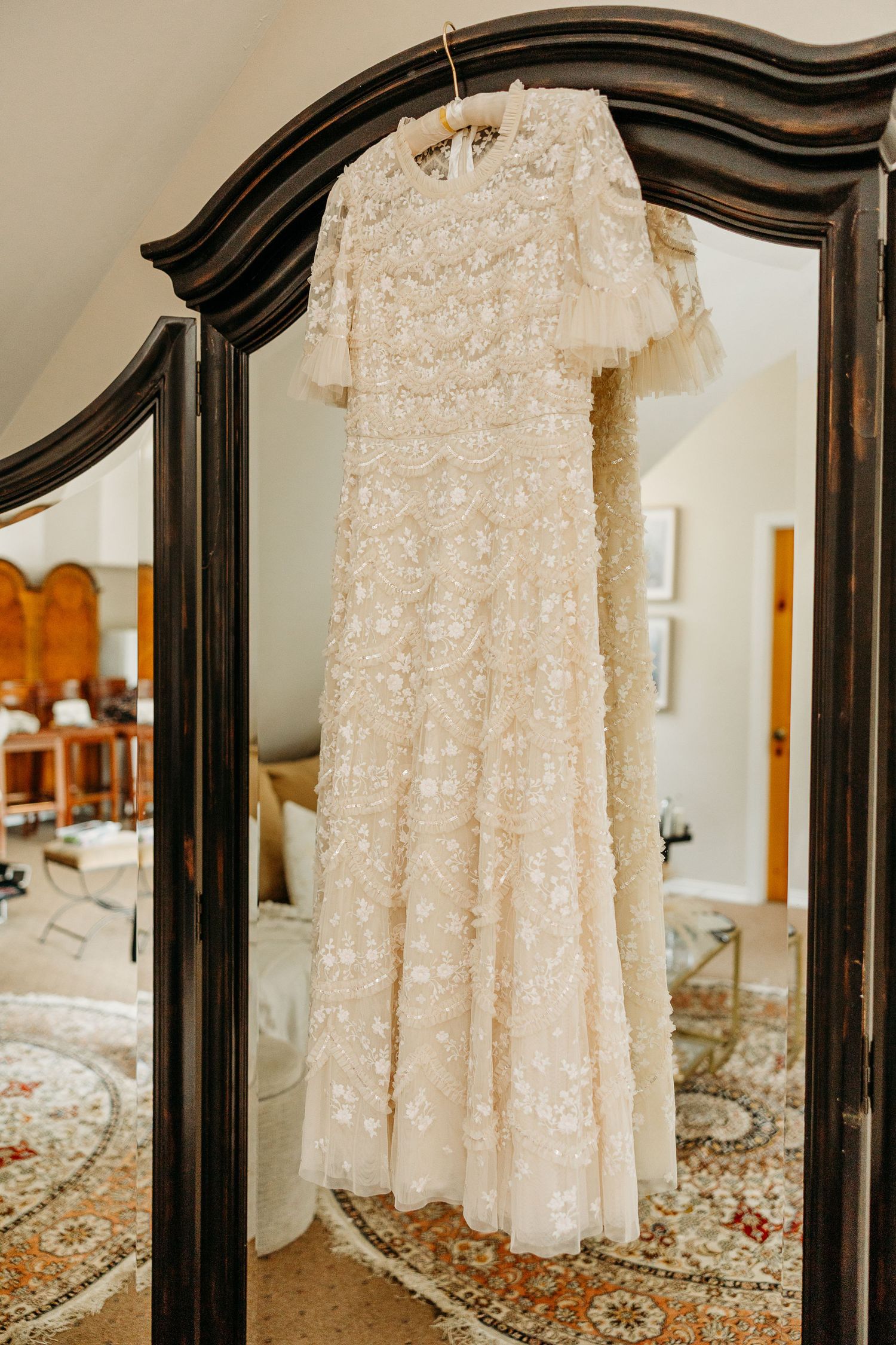 Delicate white lace wedding dress hanging on dark wooden hangers against a light wall.