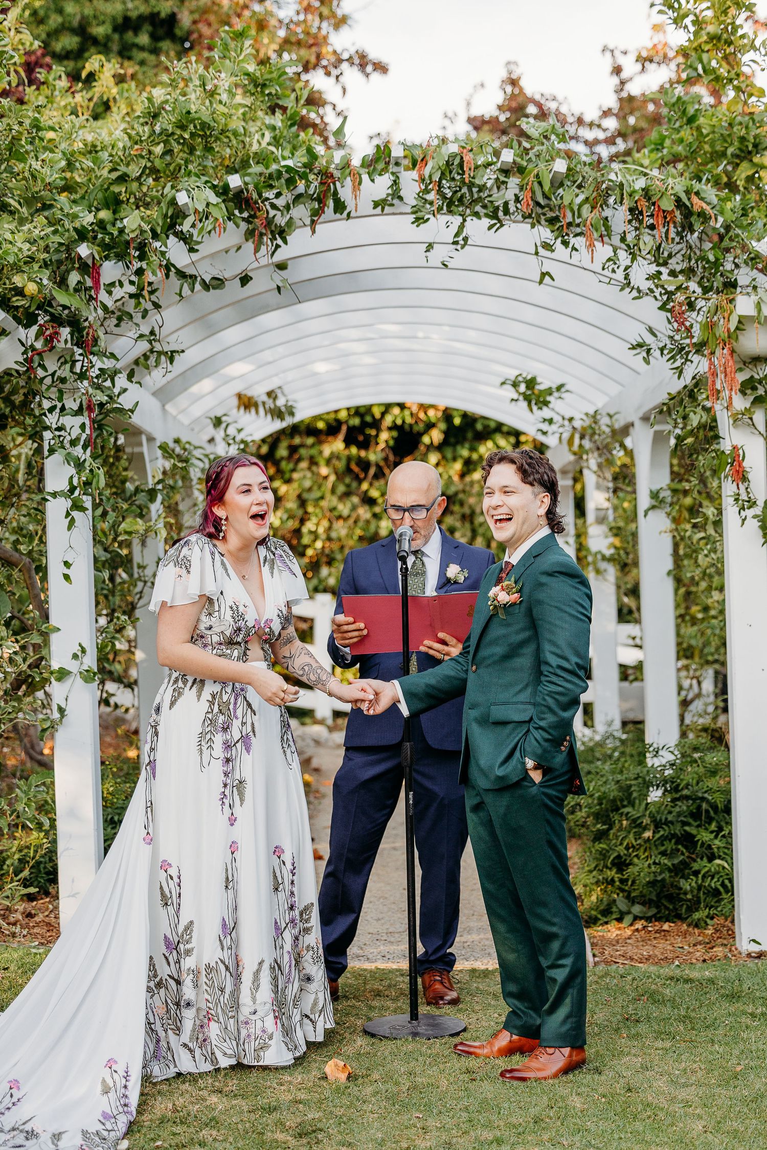A joyful wedding ceremony under a white garden pergola with climbing vines and flowers.