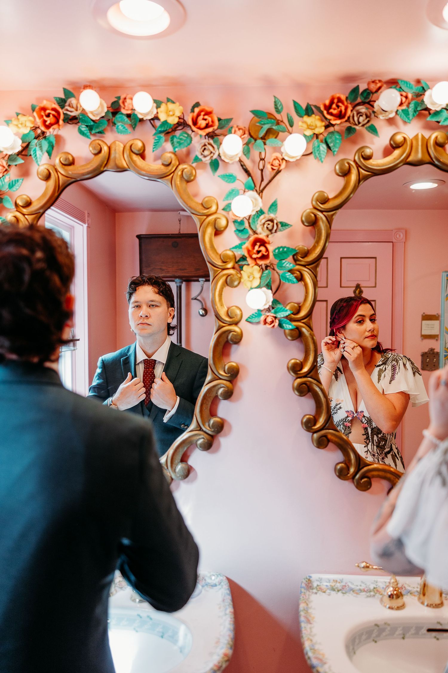 Wedding party getting ready in front of an ornate mirror decorated with floral accents.