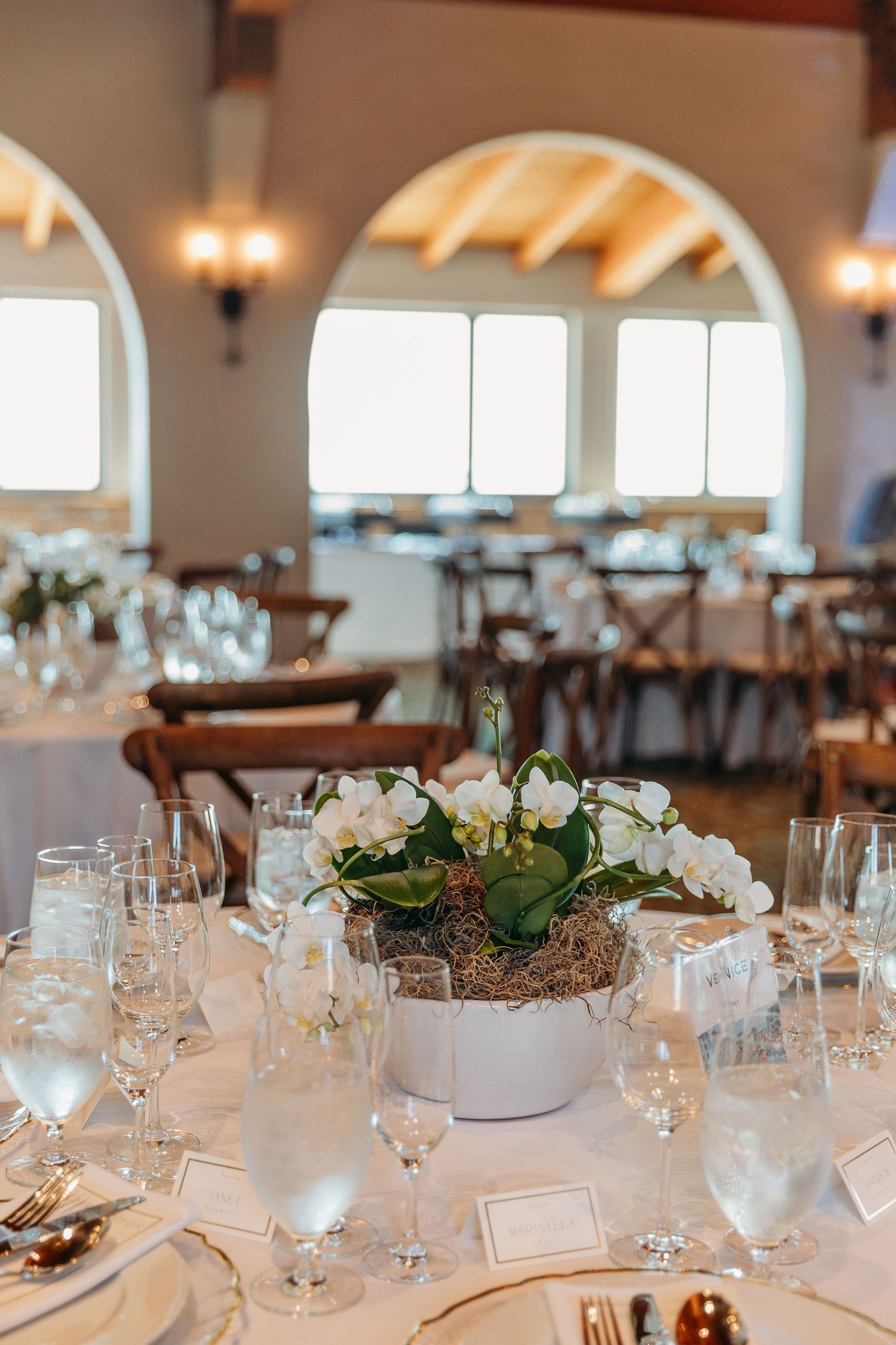 Elegant wedding reception table setting with white orchid centerpiece and arched windows.
