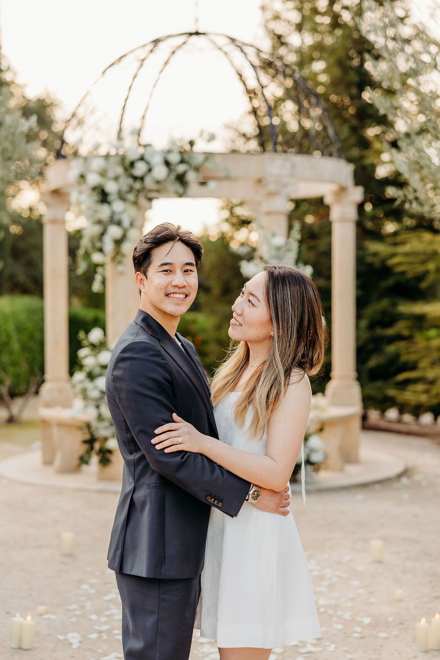 A joyful moment captured beneath an ornate garden gazebo decorated with white flowers.