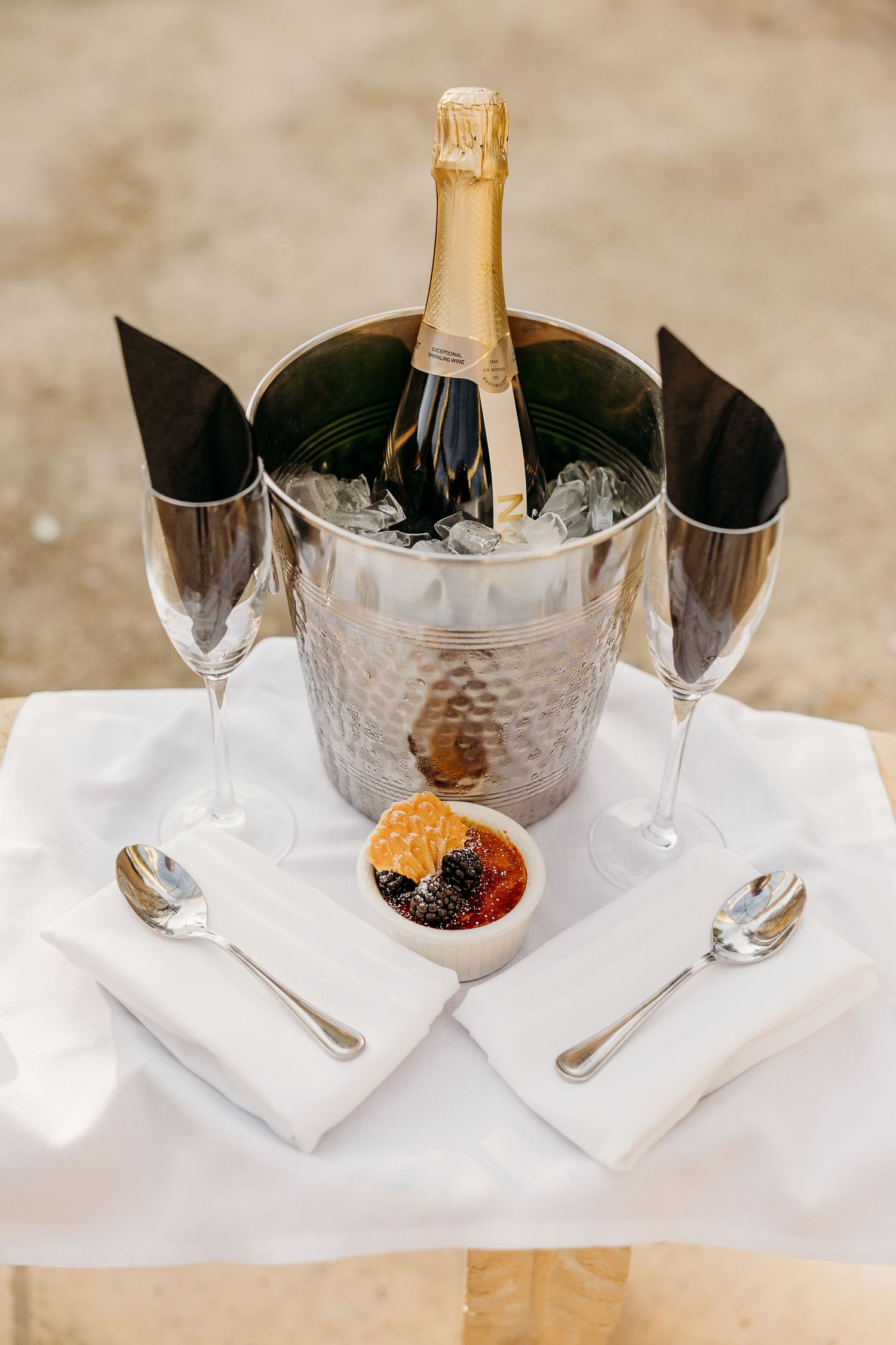 Champagne bottle chilling in silver ice bucket with elegant place settings on white tablecloth.