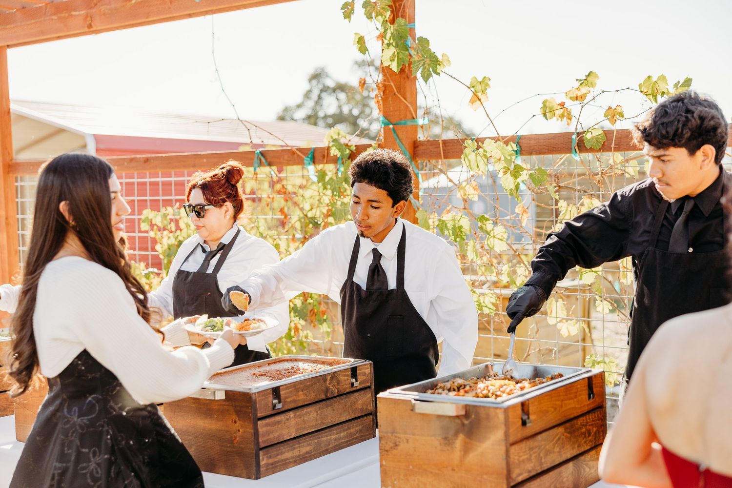 Wedding guests seated at rustic wooden tables under covered outdoor venue.