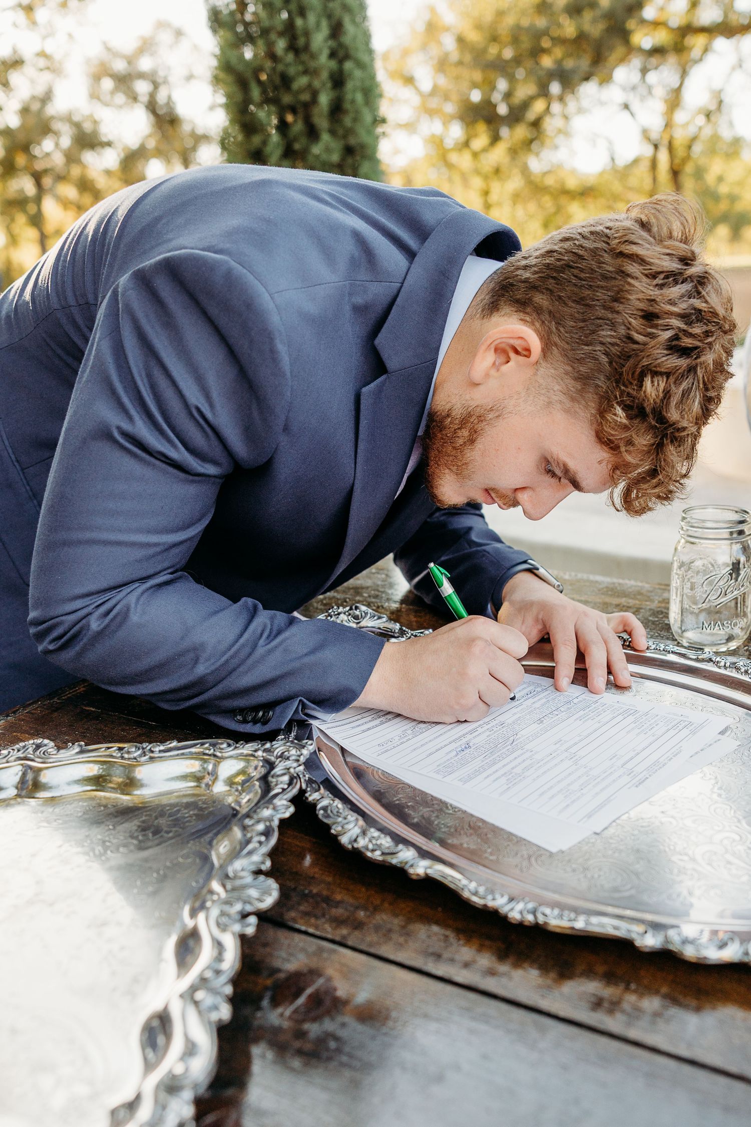 Close-up of wedding document being signed on decorative silver platter.