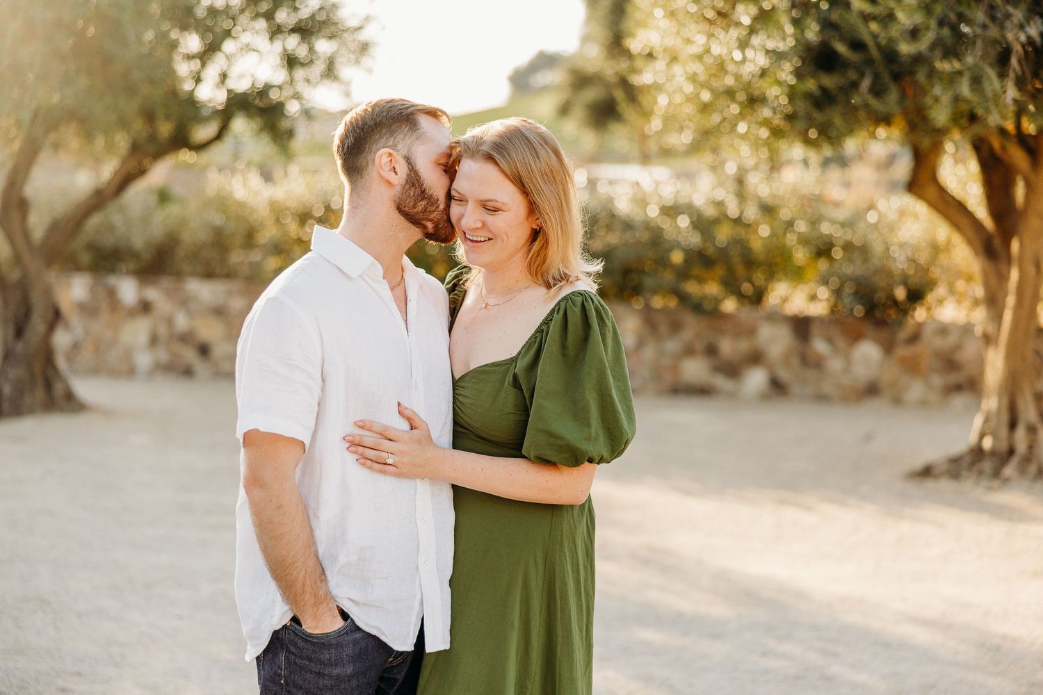 A couple embraces in a sun-drenched outdoor setting with natural desert landscape and golden light in the background.