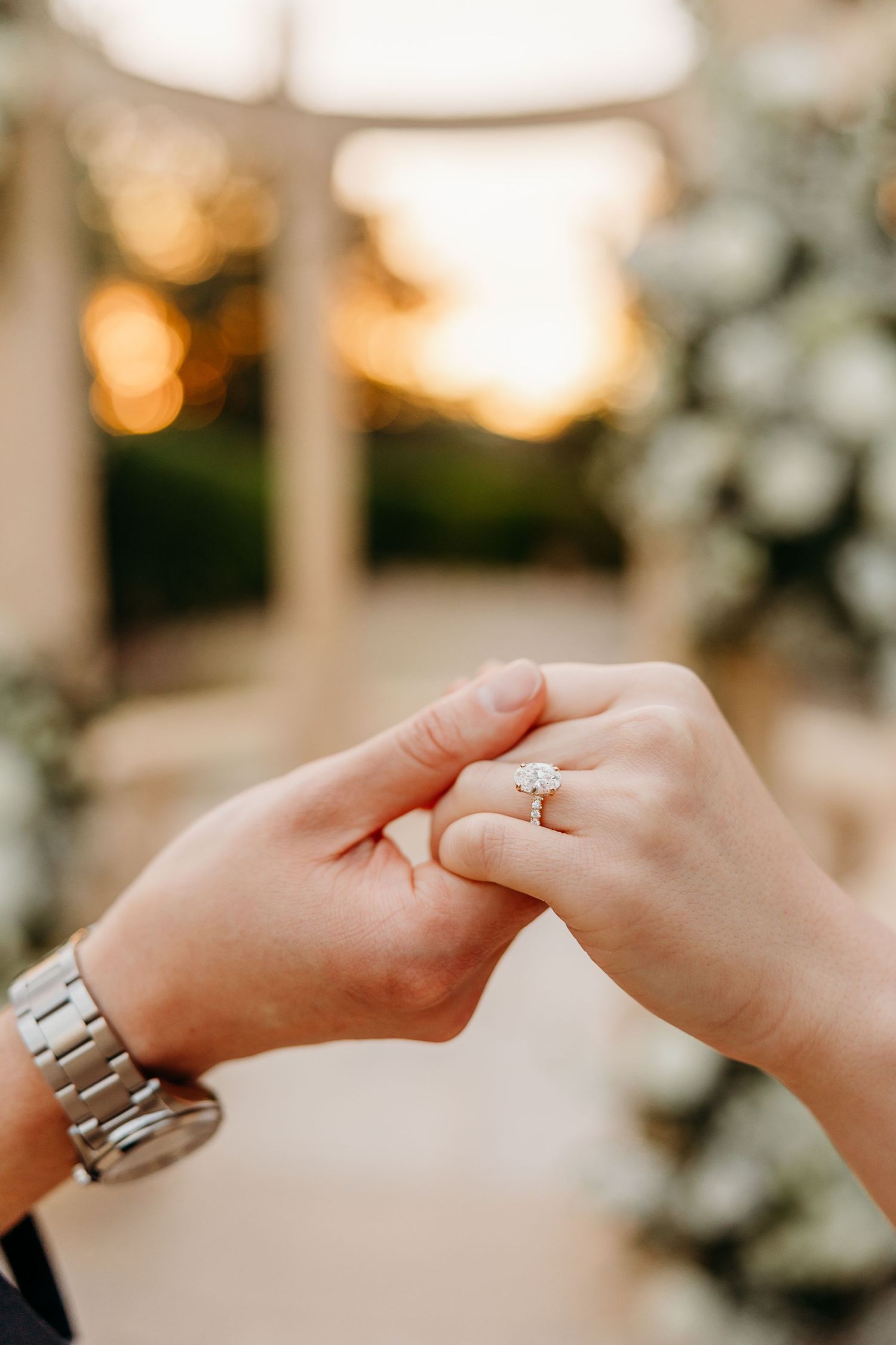 Detail shot of hands with wedding rings reaching towards each other against sunset background.