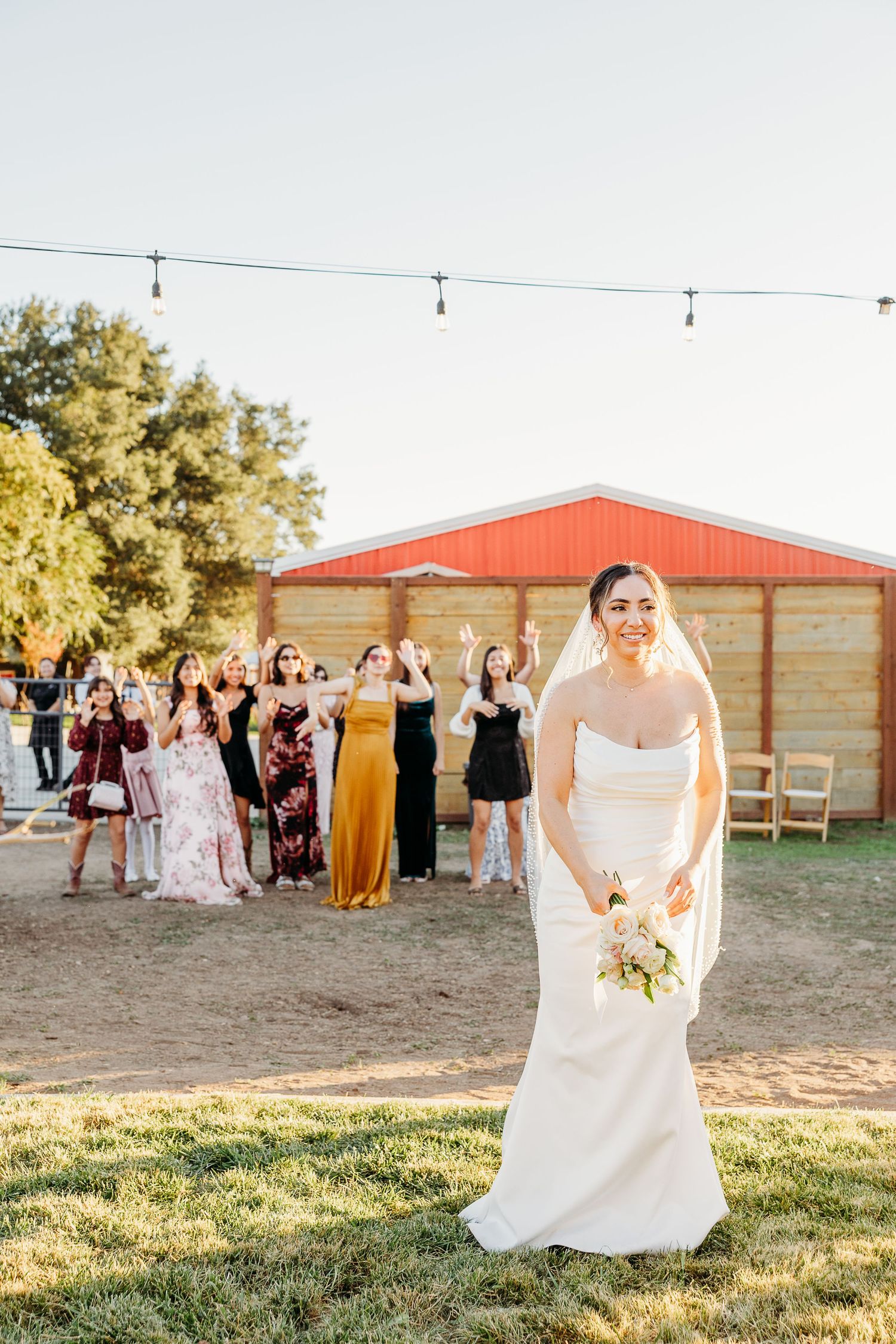 Outdoor wedding celebration at rustic red barn venue with string lights.