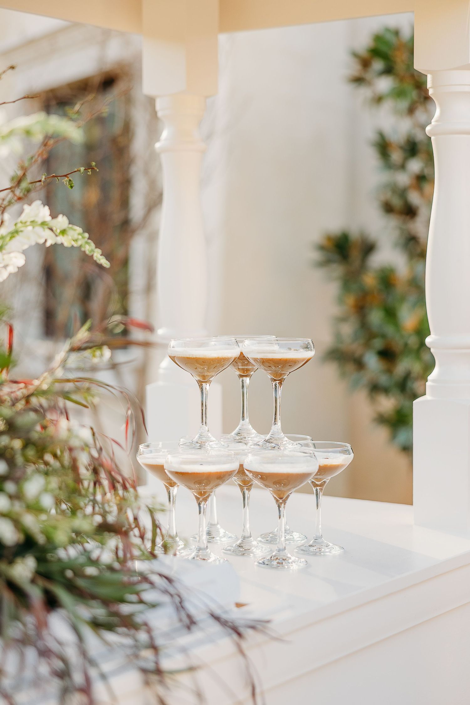 Elegant champagne glasses arranged on white shelves with soft floral decorations in the background.