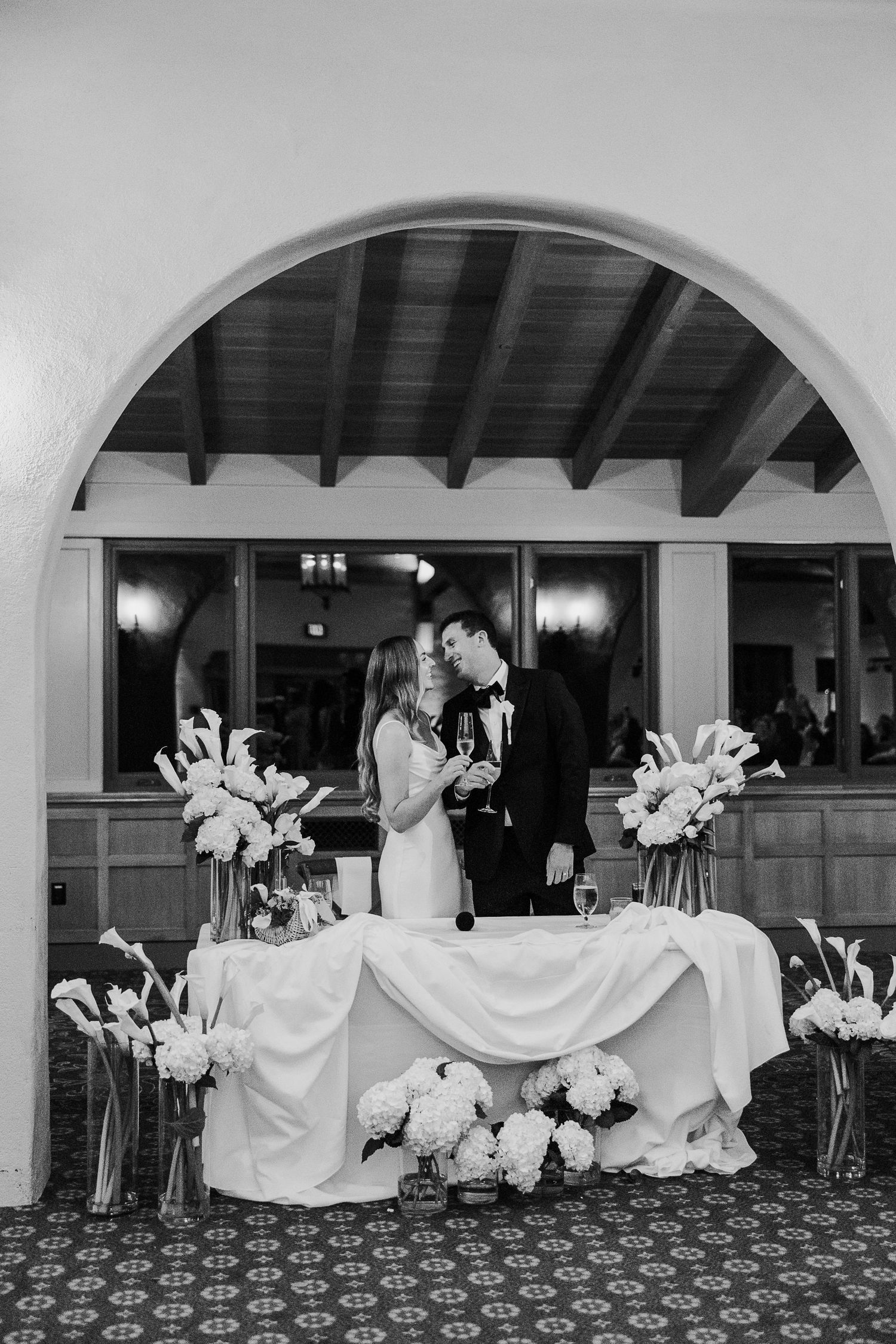 Wedding reception setup under arched doorways with white floral arrangements and draped fabric.