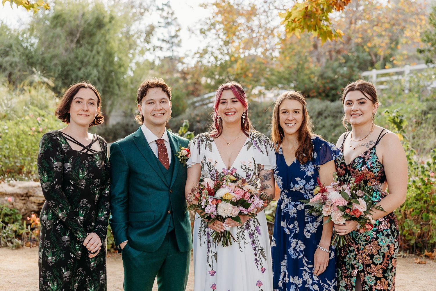 Wedding party in floral dresses and dark suits poses outdoors in autumn.