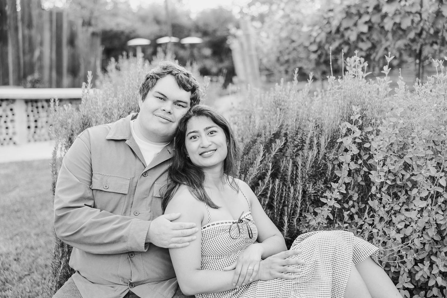 Black and white outdoor portrait of a couple sitting together and embracing on a garden bench.