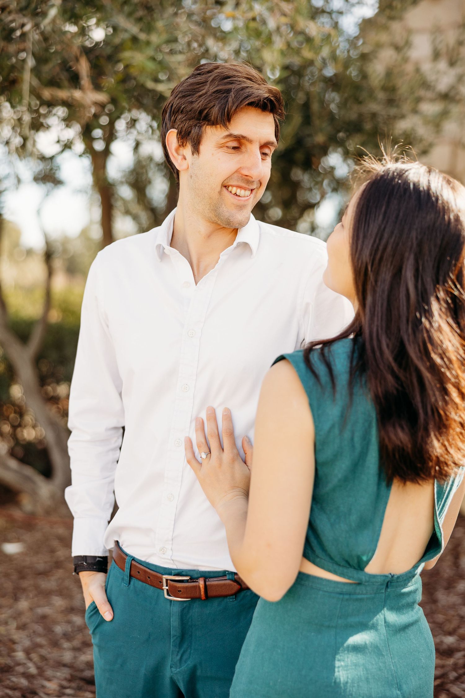 A couple shares a tender moment outdoors in contrasting white and teal outfits during a romantic photoshoot.