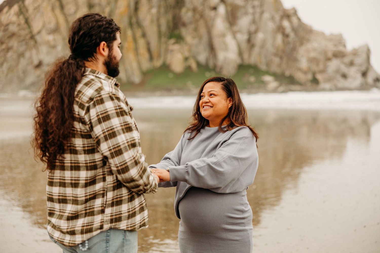 A couple shares a happy moment together on a beach with rocky cliffs in the background at sunset.