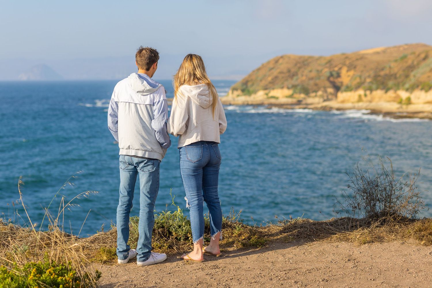 A couple stands together admiring the coastal view on a scenic cliff overlook.