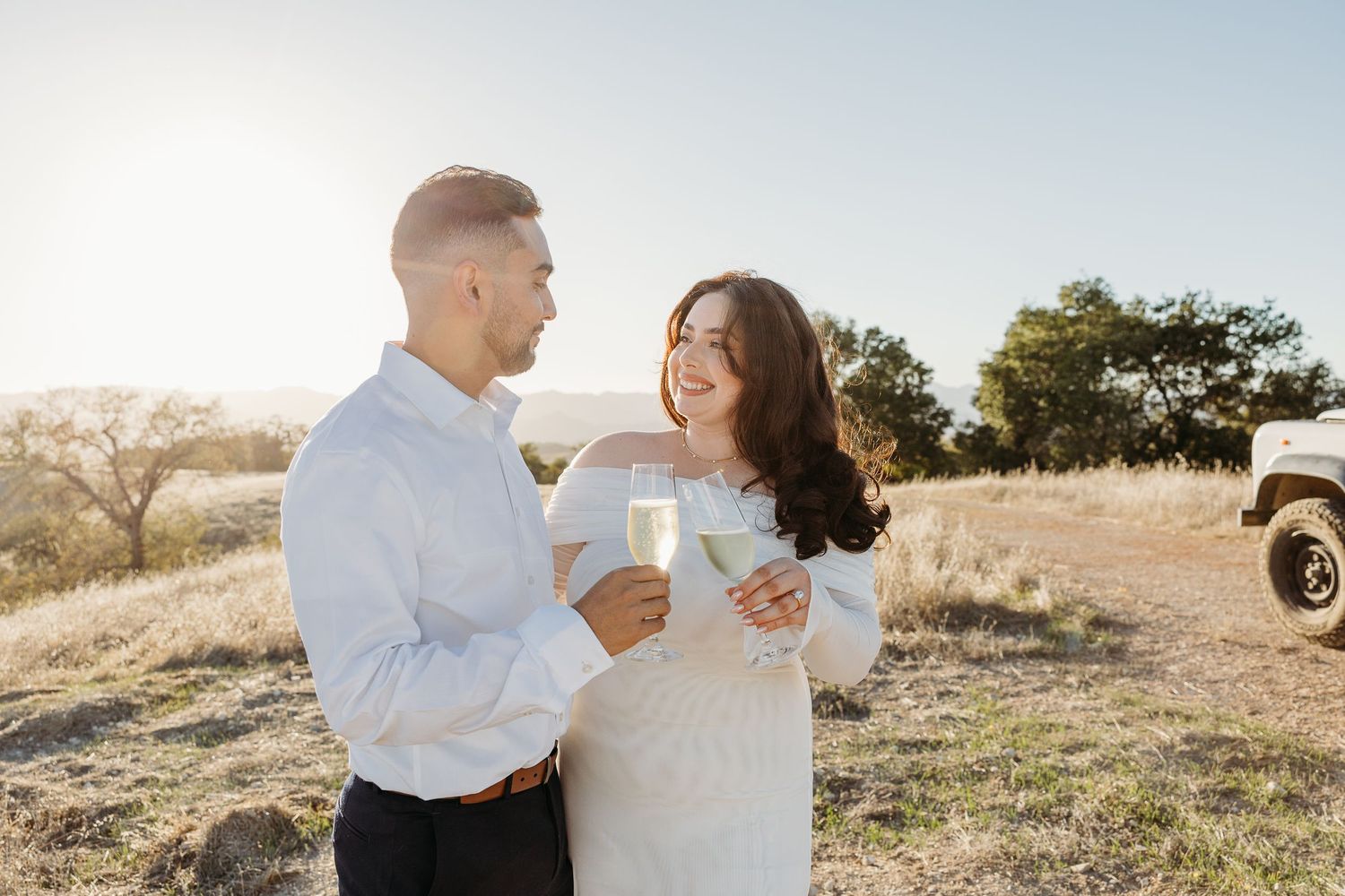 Romantic couple embraces in golden sunlit field during sunset engagement photo session.