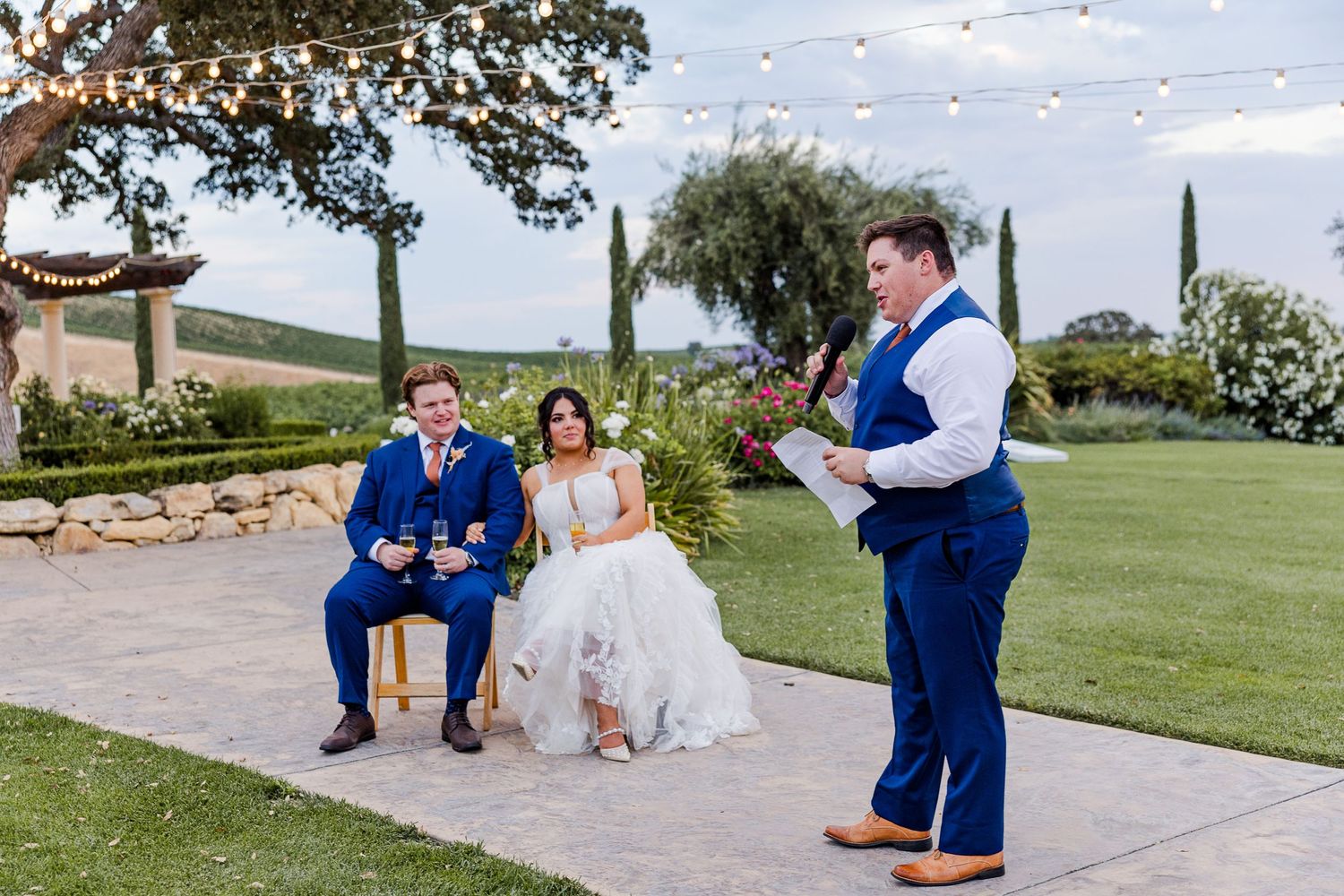 Wedding celebration on a manicured lawn with string lights overhead.