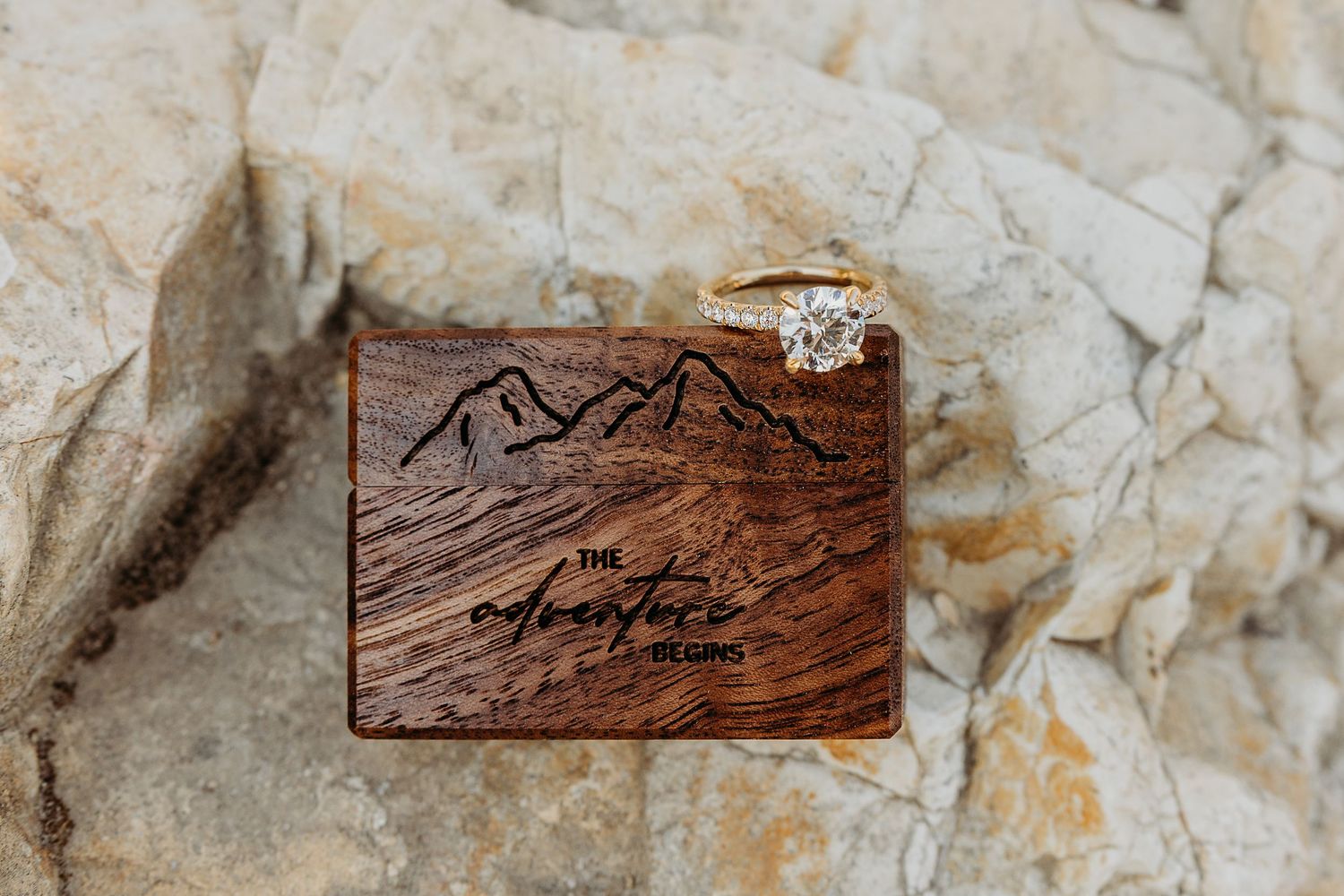 Close-up of an engagement ring displayed on textured stone with carved wooden decor.