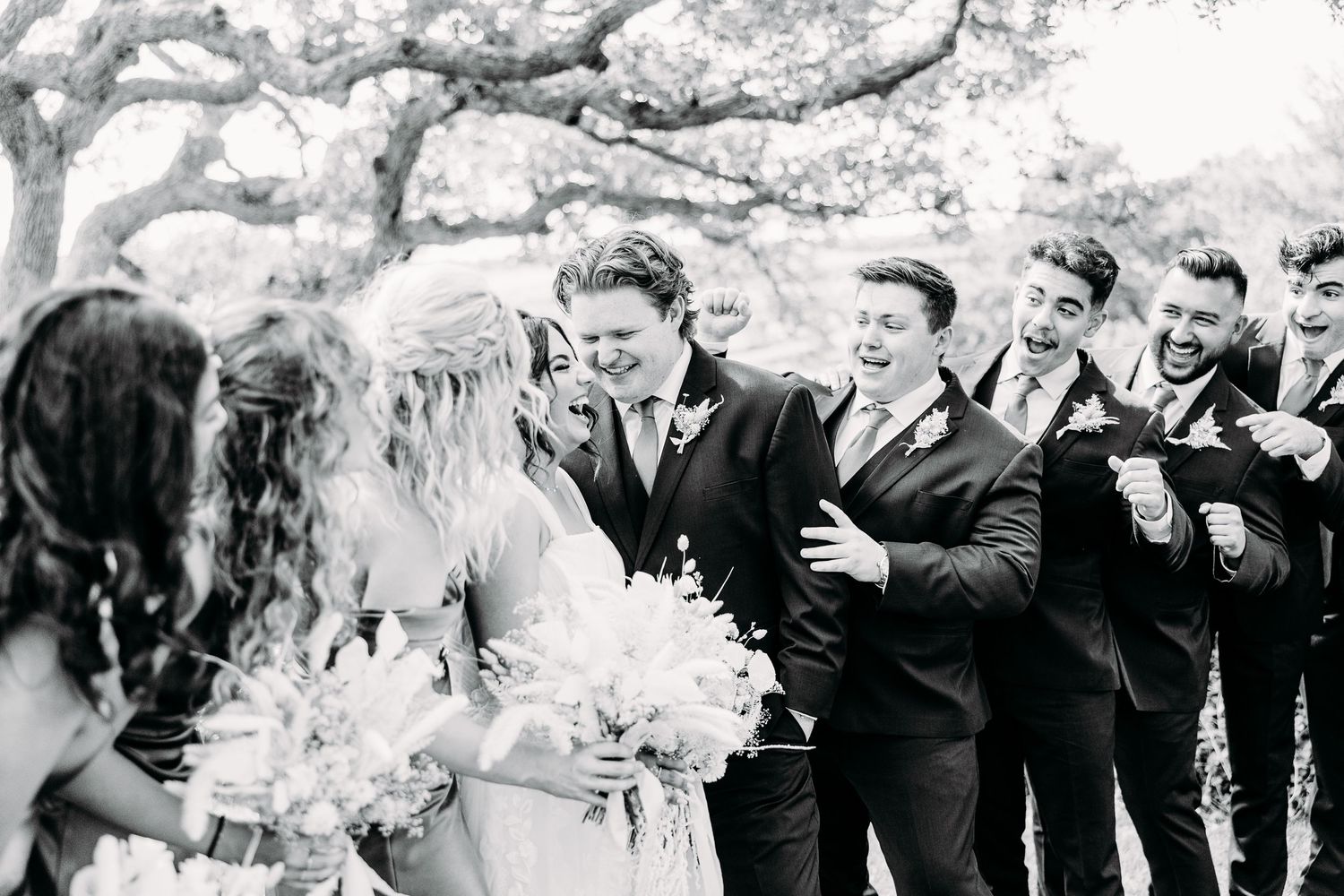 Black and white photo of a wedding celebration with bridesmaids and groomsmen outdoors.