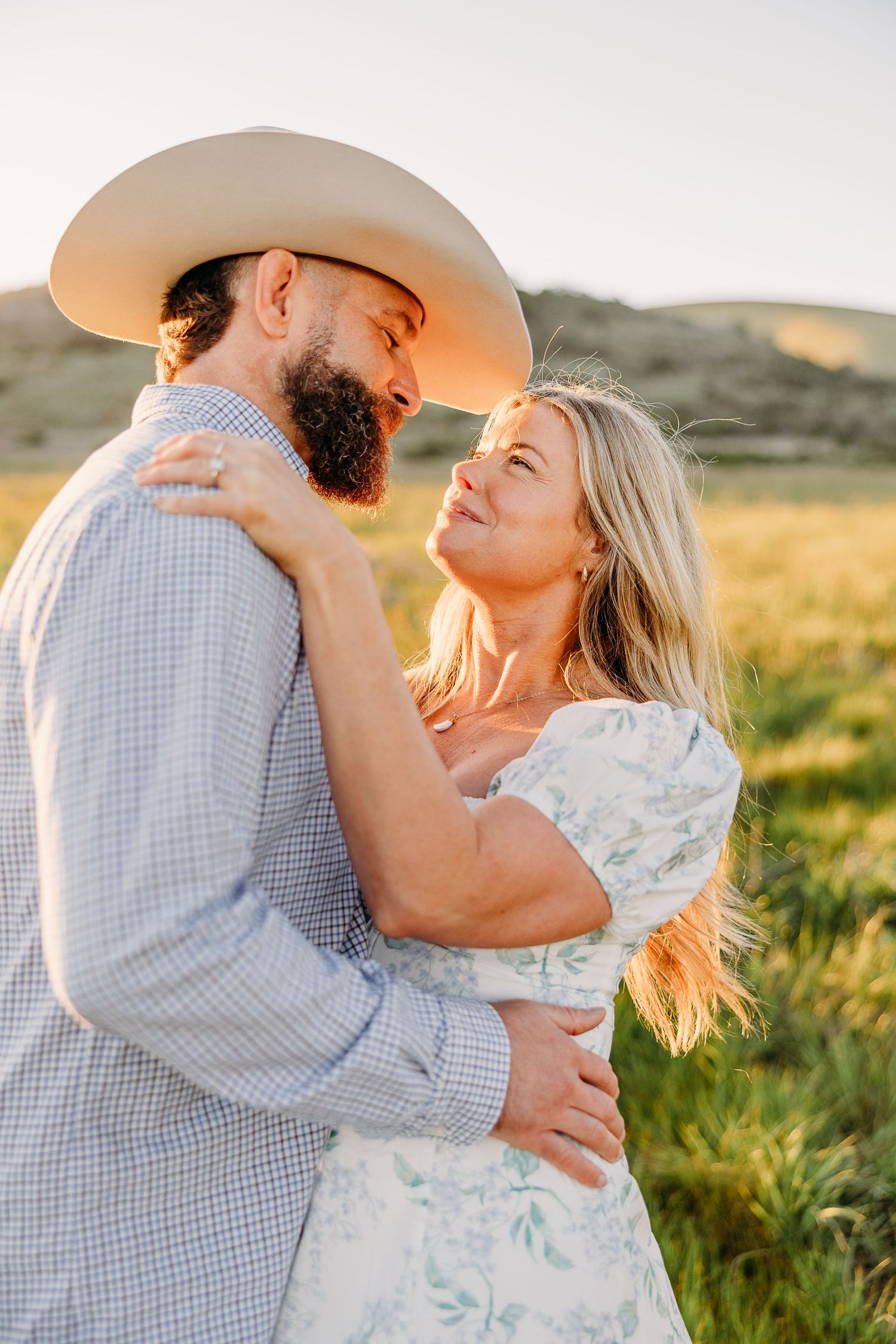 A couple in casual attire shares a tender moment in a sun-drenched field at golden hour.