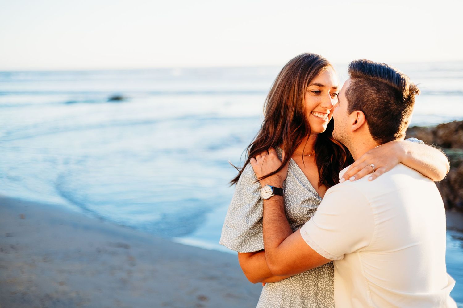 A joyful couple laughs together while embracing near the ocean waves.