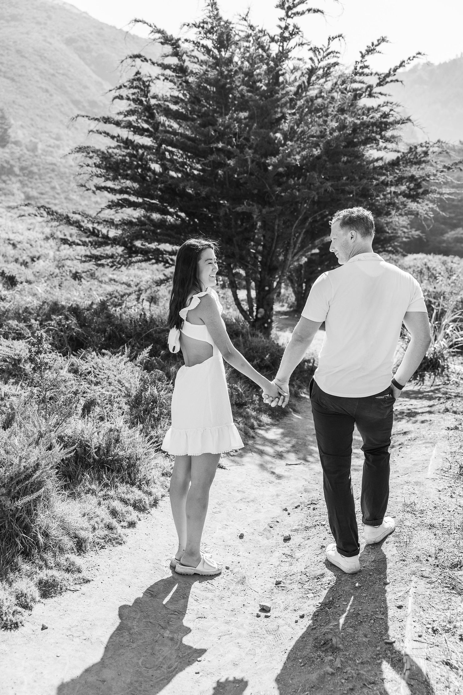 Black and white photo of a couple holding hands while walking on a mountain trail.
