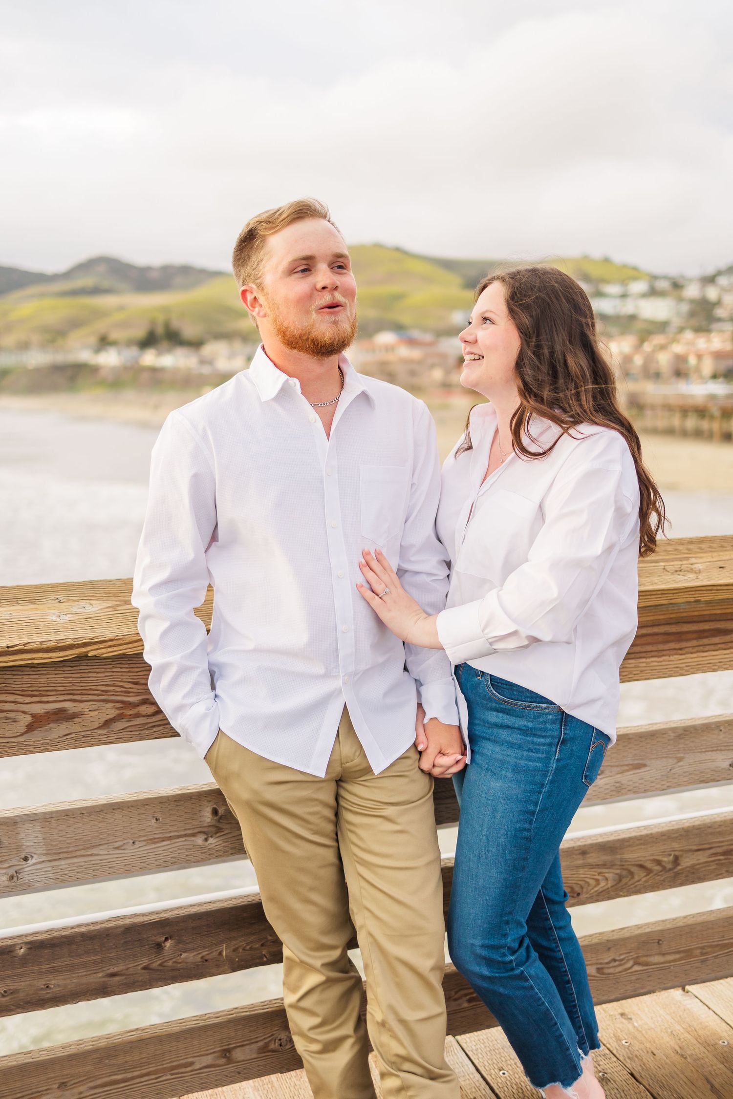 Happy couple in coordinated outfits sharing intimate moment on beach pier.