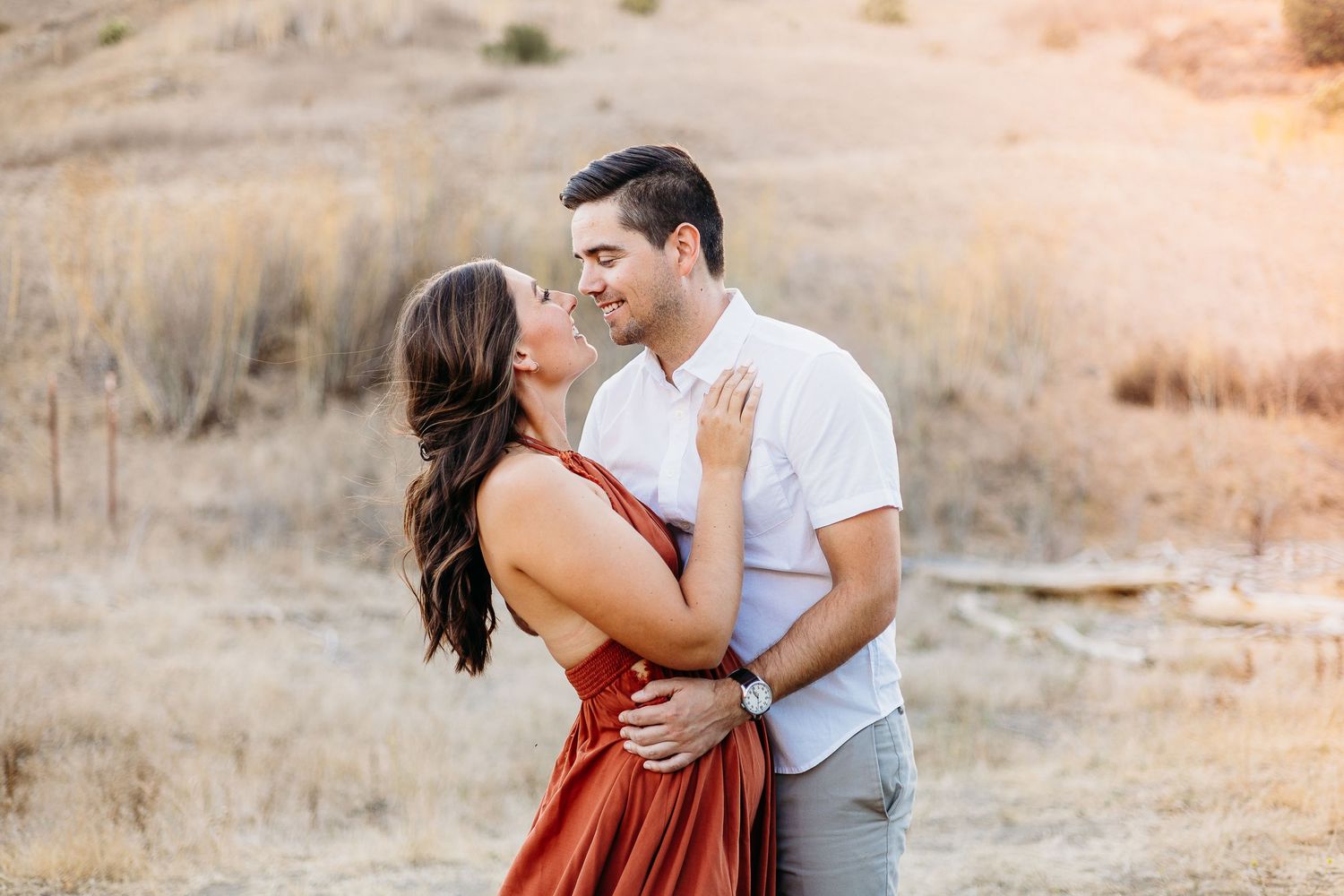 Romantic couple embraces in a rustic outdoor setting with golden hills at sunset.