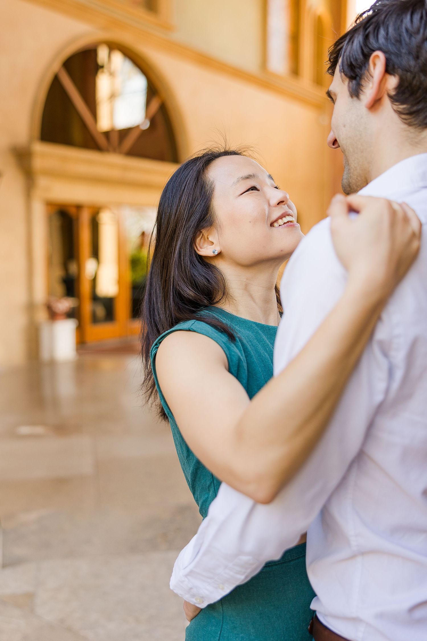 A romantic couple embracing and smiling in an elegant archway-lined hallway.