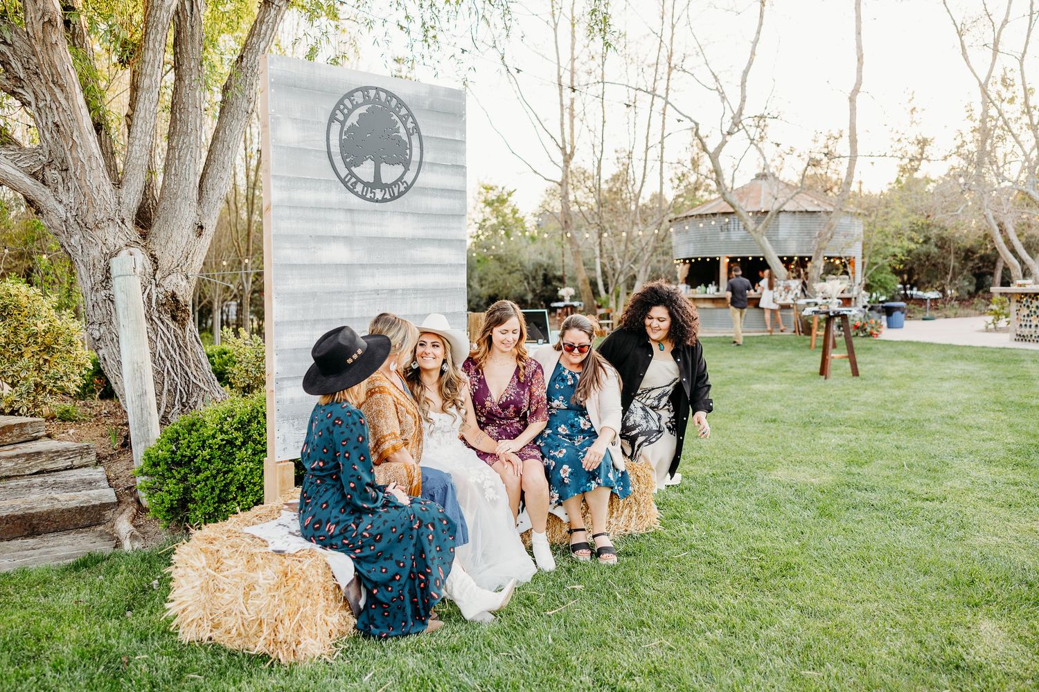 A group of wedding guests seated on hay bales enjoying a casual outdoor celebration.