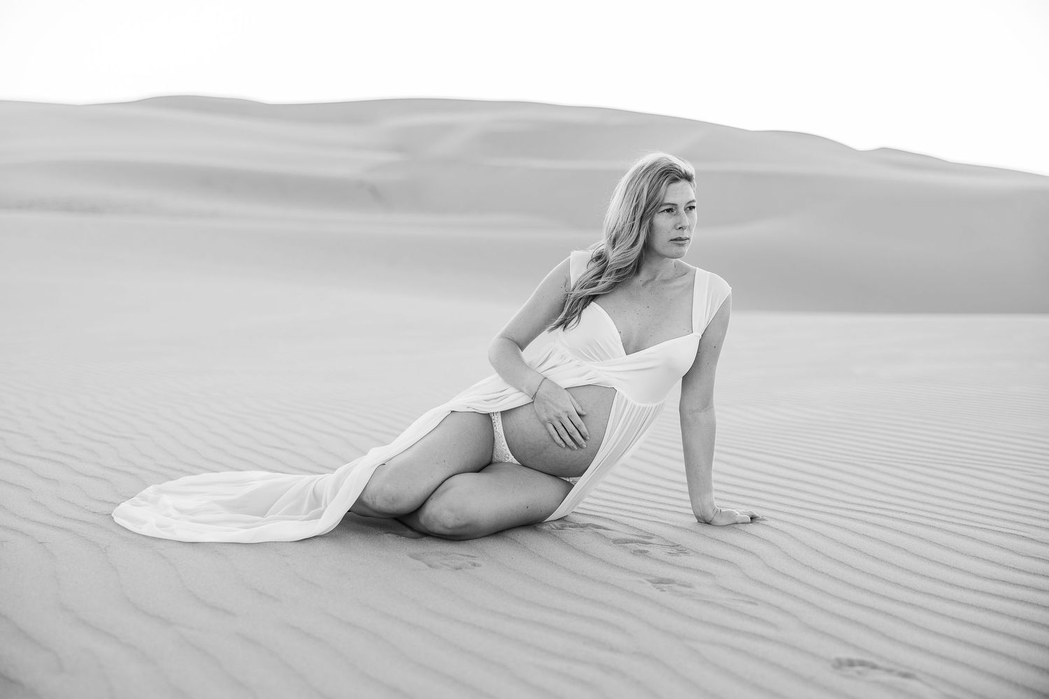 Black and white maternity portrait on desert dunes with artistic composition.