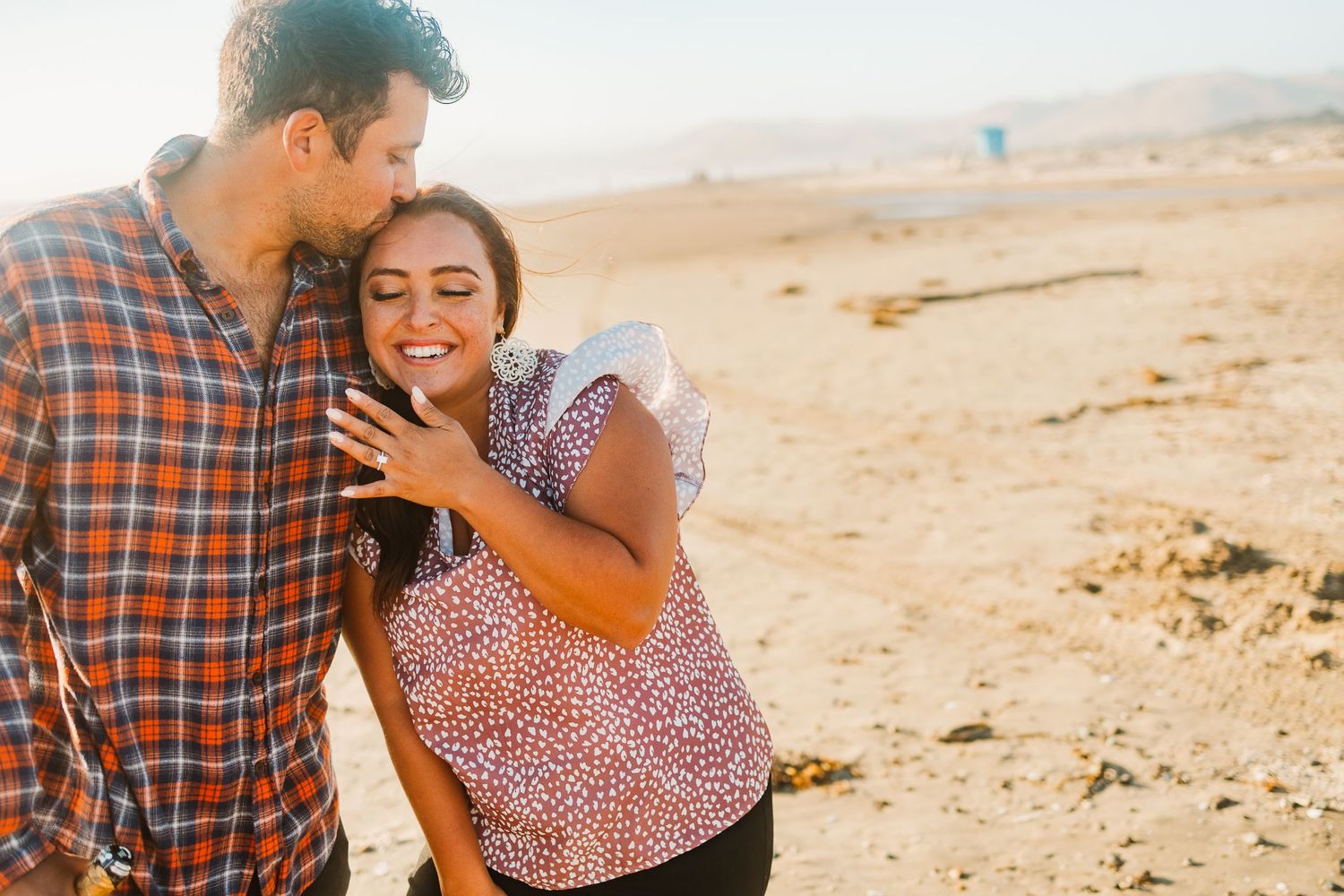 Joyful couple sharing exciting moment on beach while showing off engagement ring.