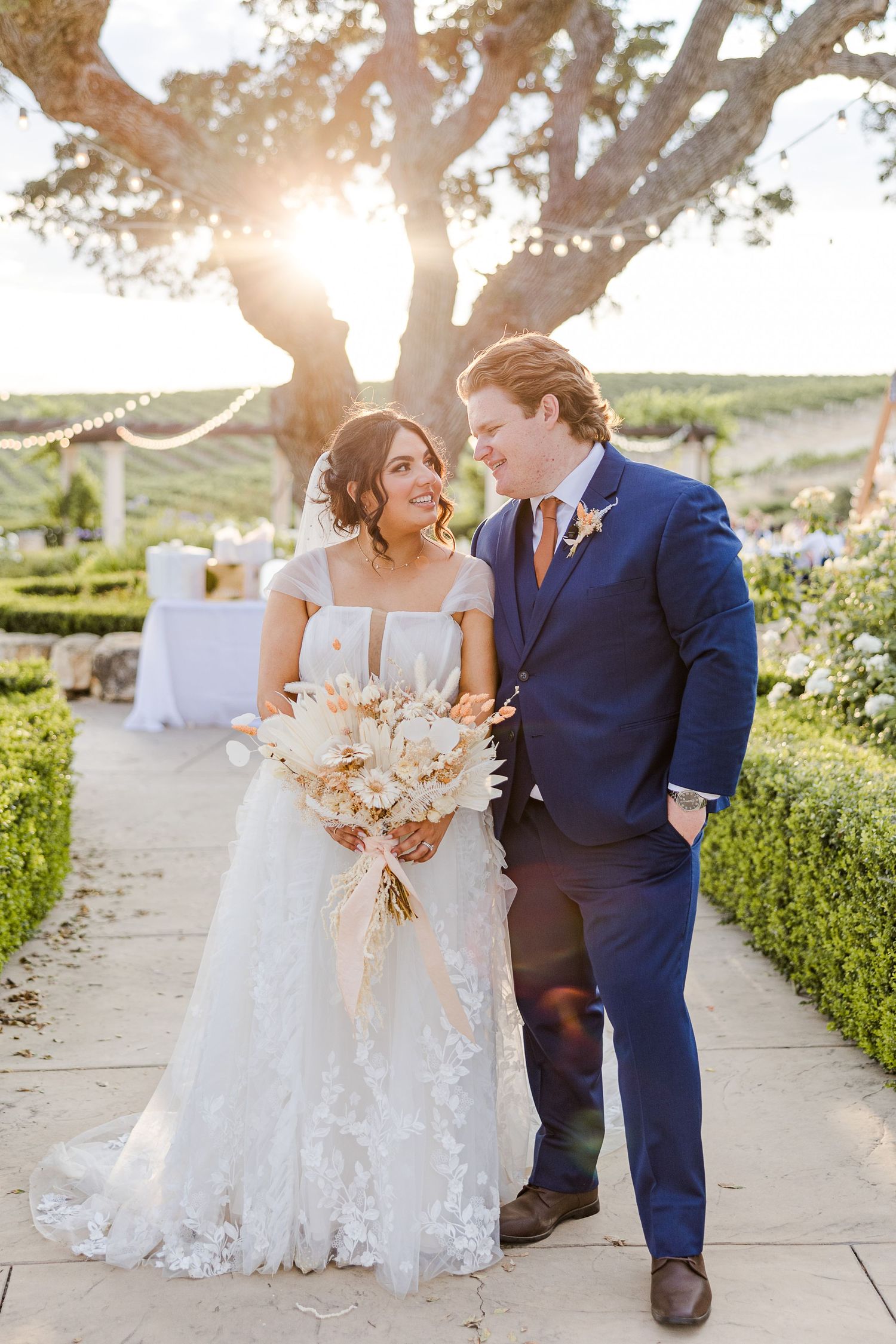 Sunset wedding portrait with couple walking together holding neutral floral bouquet.