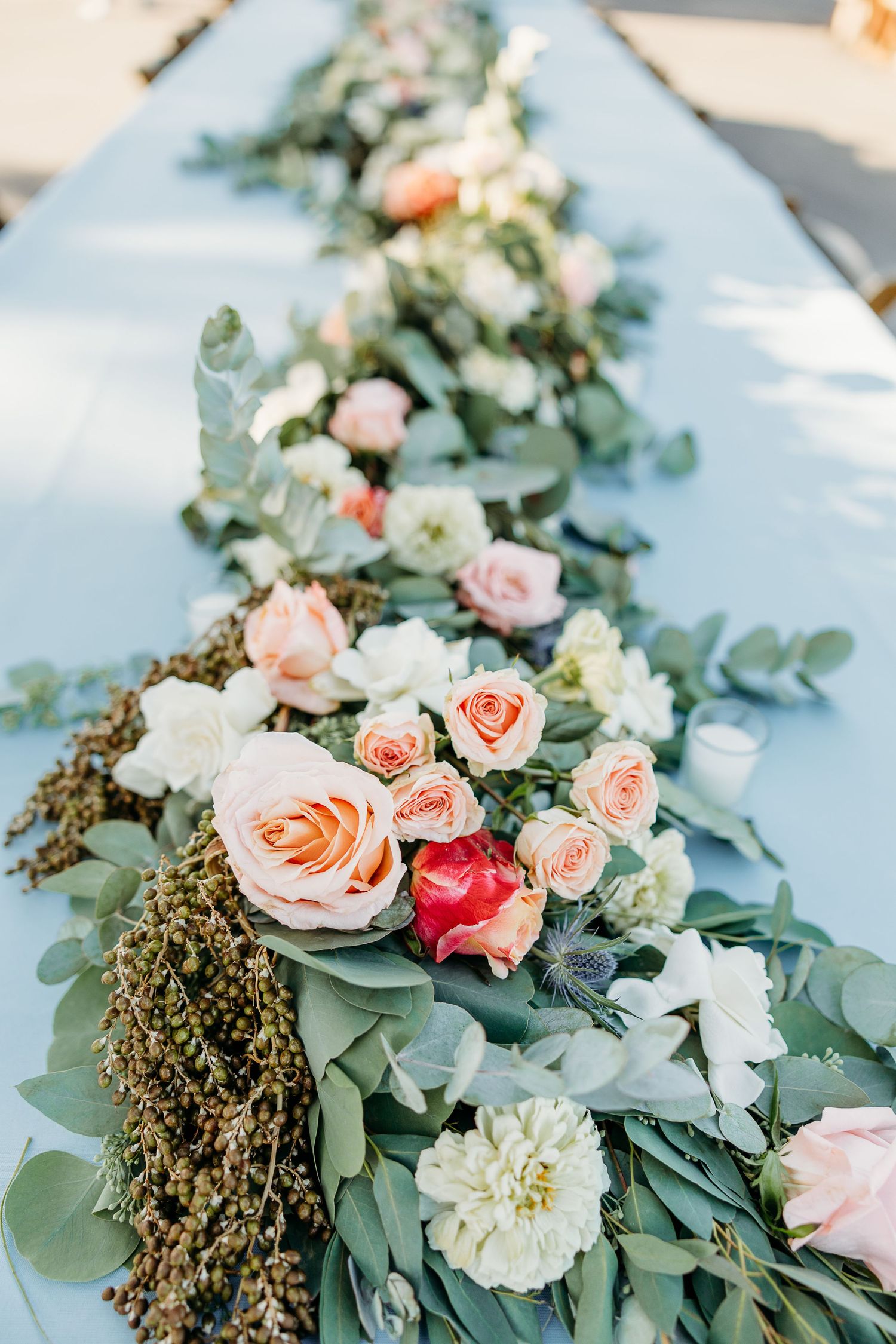 A stunning floral table runner with peach roses, white blooms and eucalyptus leaves arranged on a light blue surface at Holland Ranch SLO.