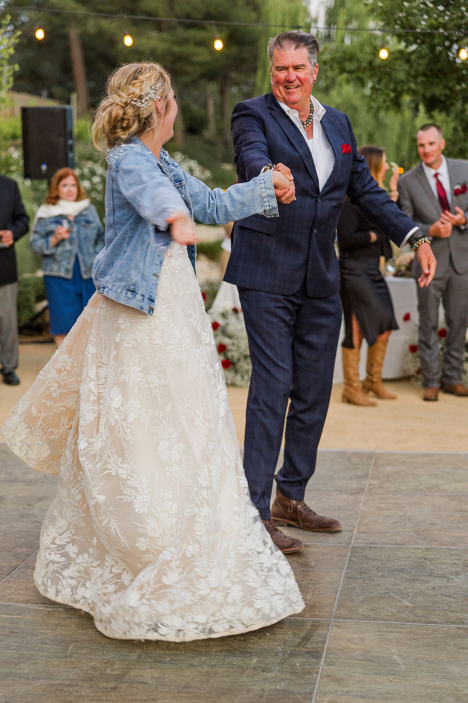 Couple dances at outdoor wedding reception with bride wearing lace gown and denim jacket.