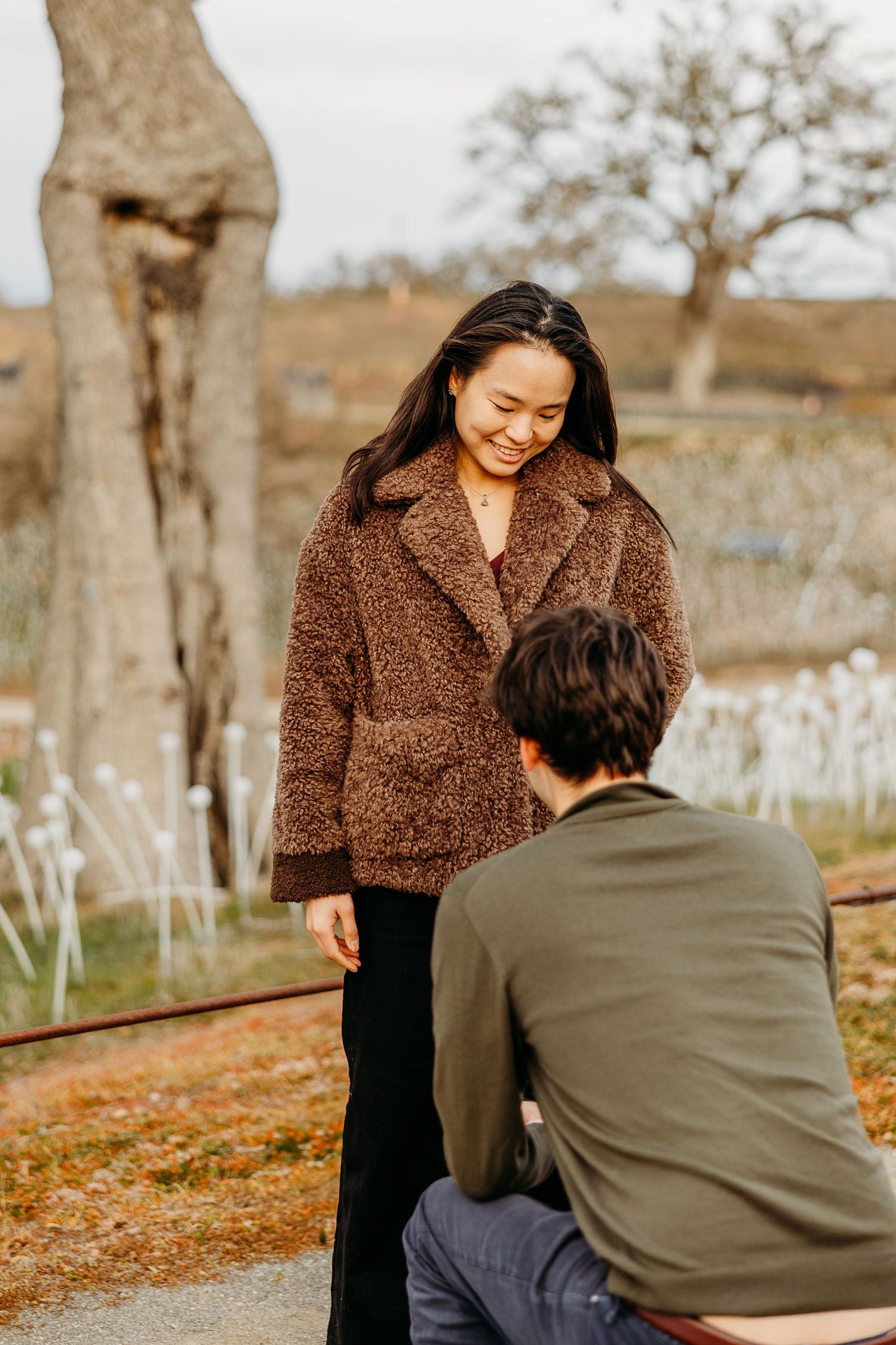 A couple shares a romantic moment together in an autumn outdoor setting with fallen leaves and bare trees.