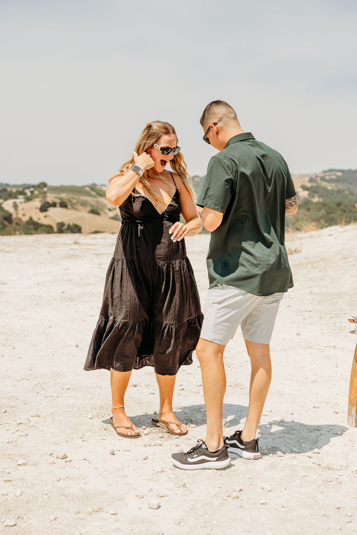 Two people share an intimate moment on a bright sandy beach surrounded by nature.