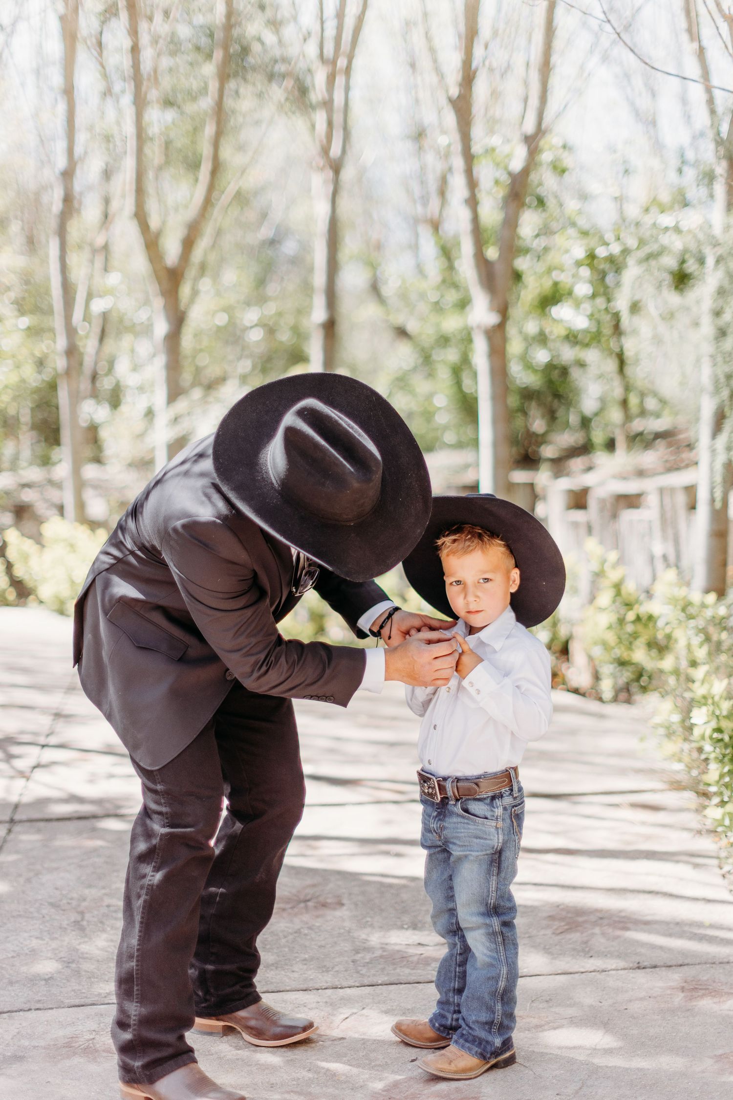 Two people in western attire and cowboy hats share a tender moment outdoors.