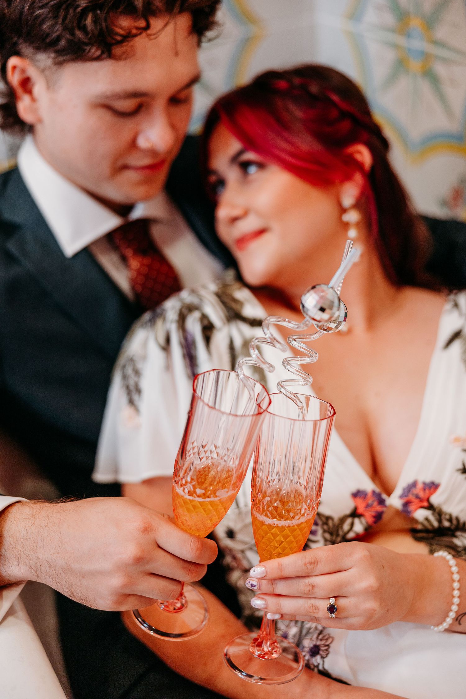 Couple toasting with crystal glasses filled with orange cocktails during celebration.