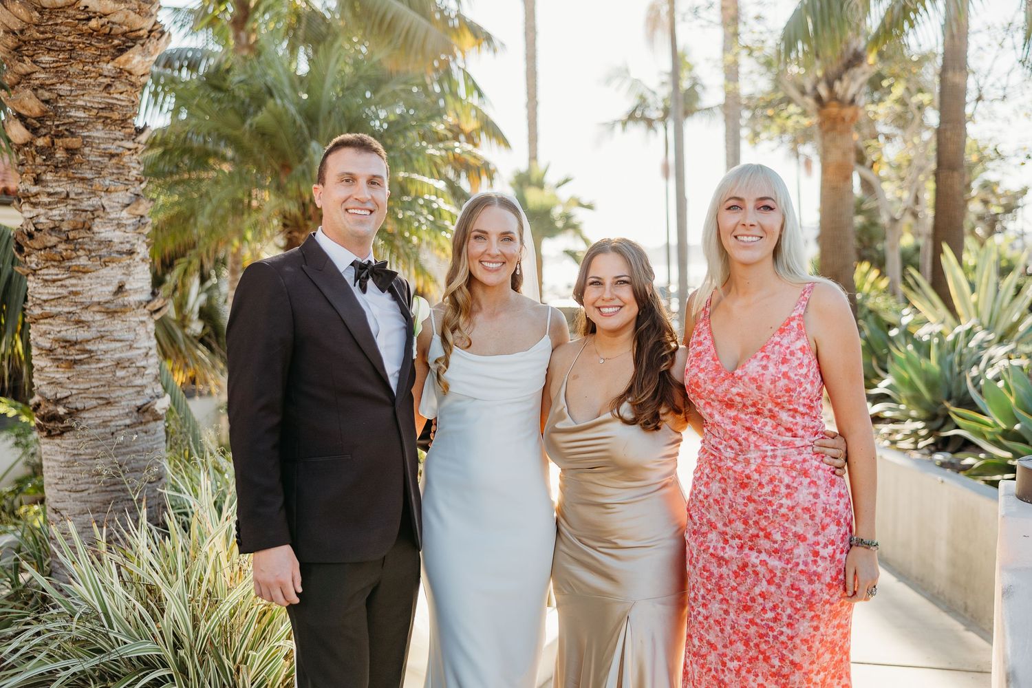 Wedding party poses together outdoors with palm trees in the background.