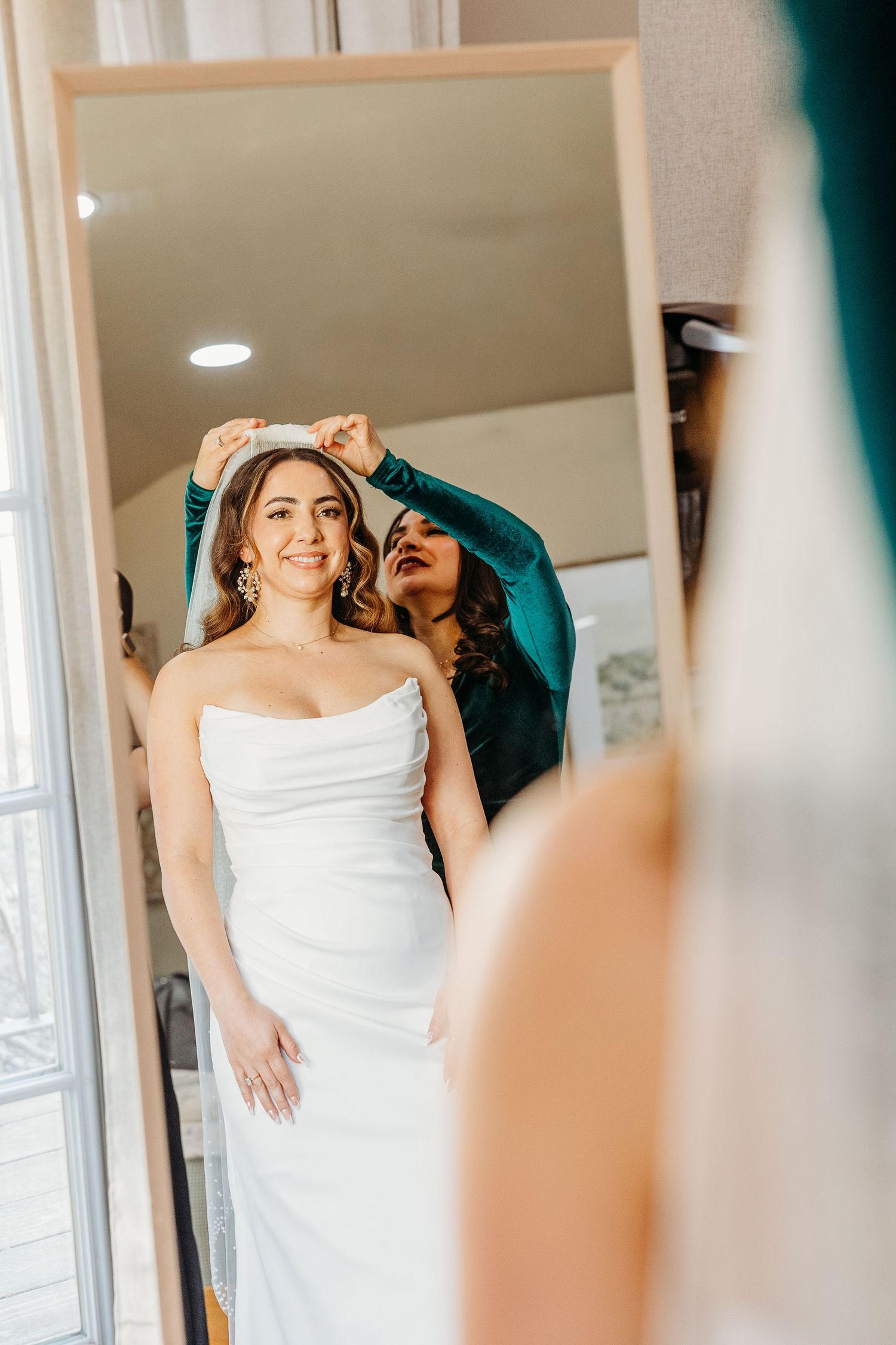 Bride in white dress getting ready in sunlit room with elegant details.