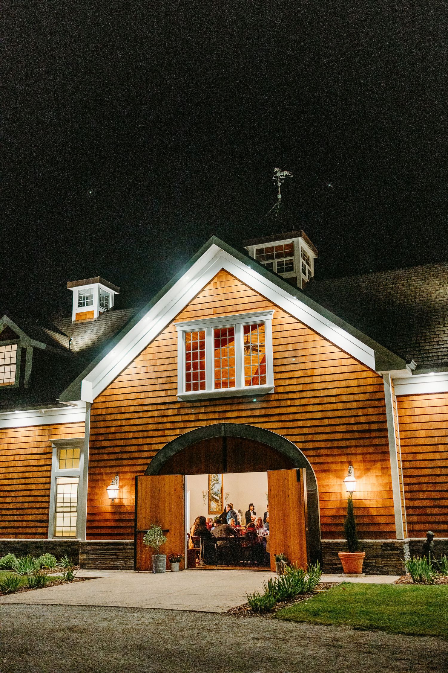 Cedar-shingled wedding venue illuminated at night with warm exterior lighting.