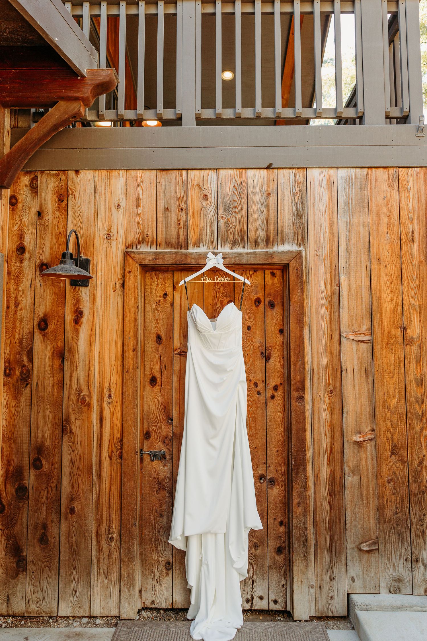 White lace wedding dress hanging on wooden wall of rustic barn venue.
