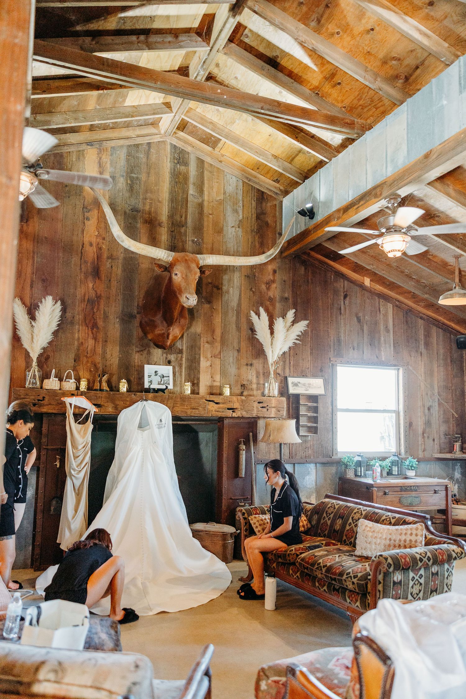 A rustic wooden cabin interior with exposed beams and white dresses hanging from the ceiling.